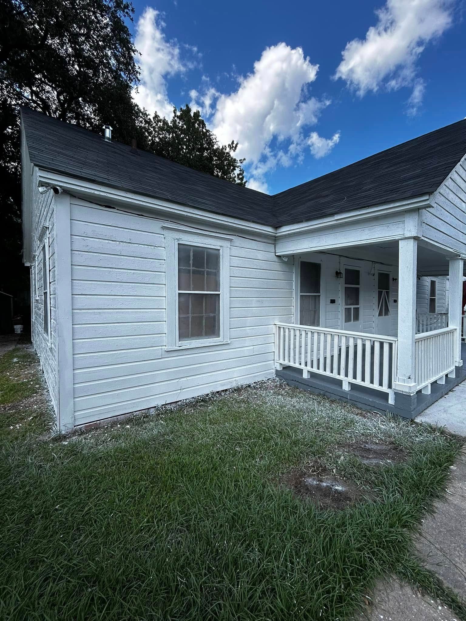 White house with a small porch and a dark roof under a cloudy sky.