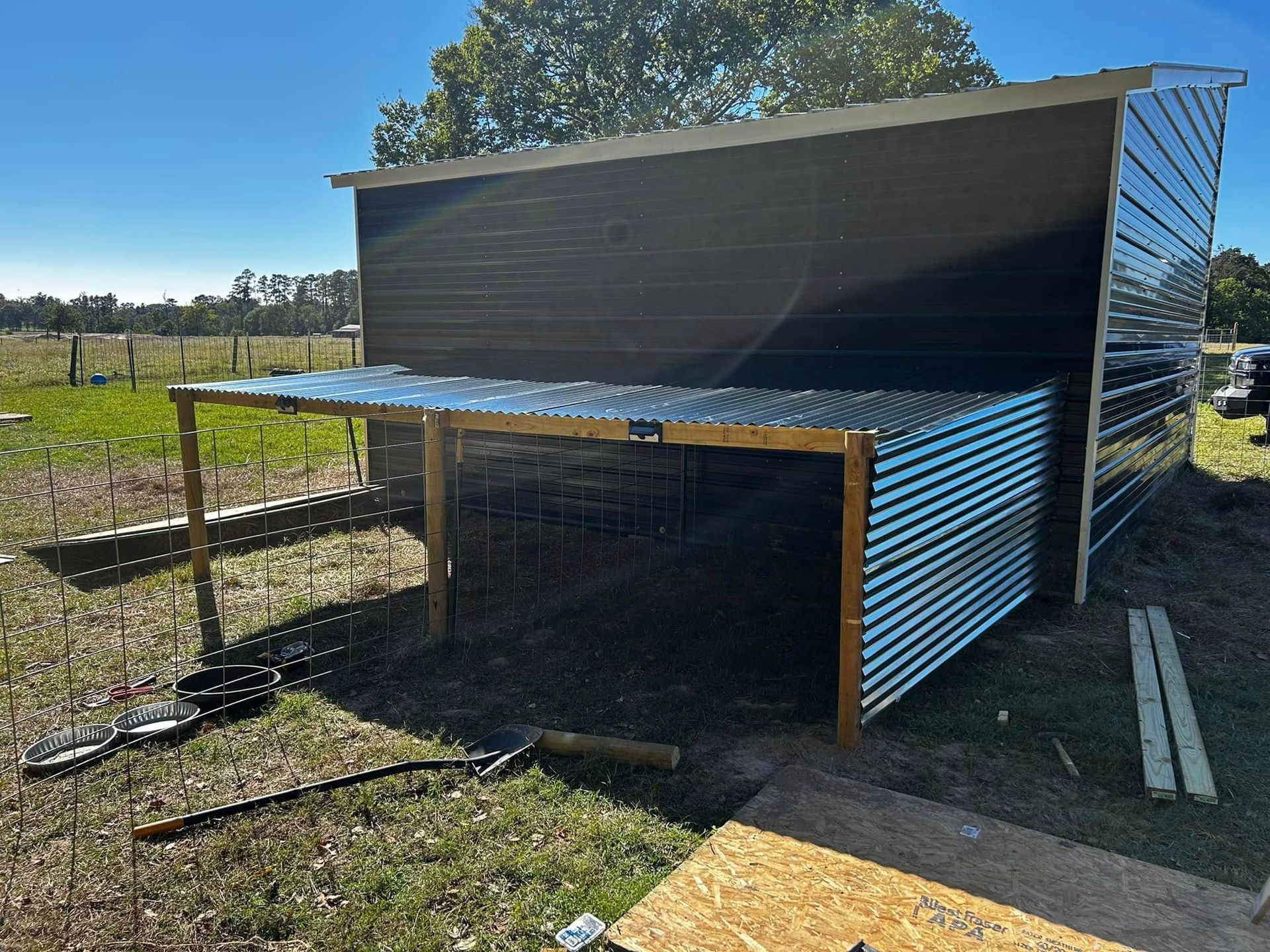 A partially constructed black and silver shelter in a grassy field on a sunny day.