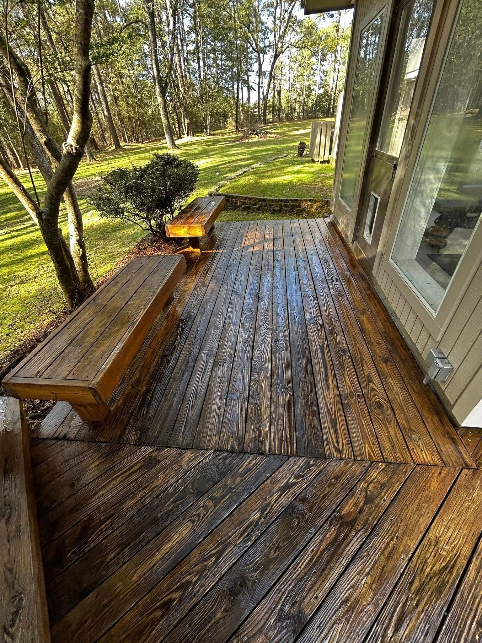Wooden deck with built-in benches, angled plank design. Overlooking a grassy yard and trees.