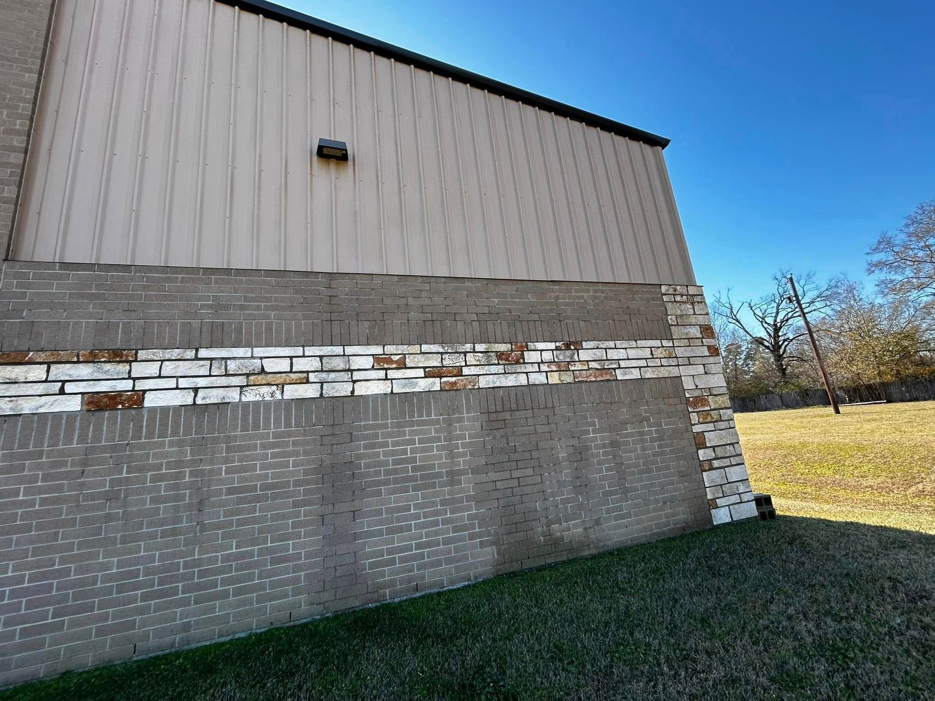 Exterior of a building with brick and stone siding, beige panels, and a blue sky.