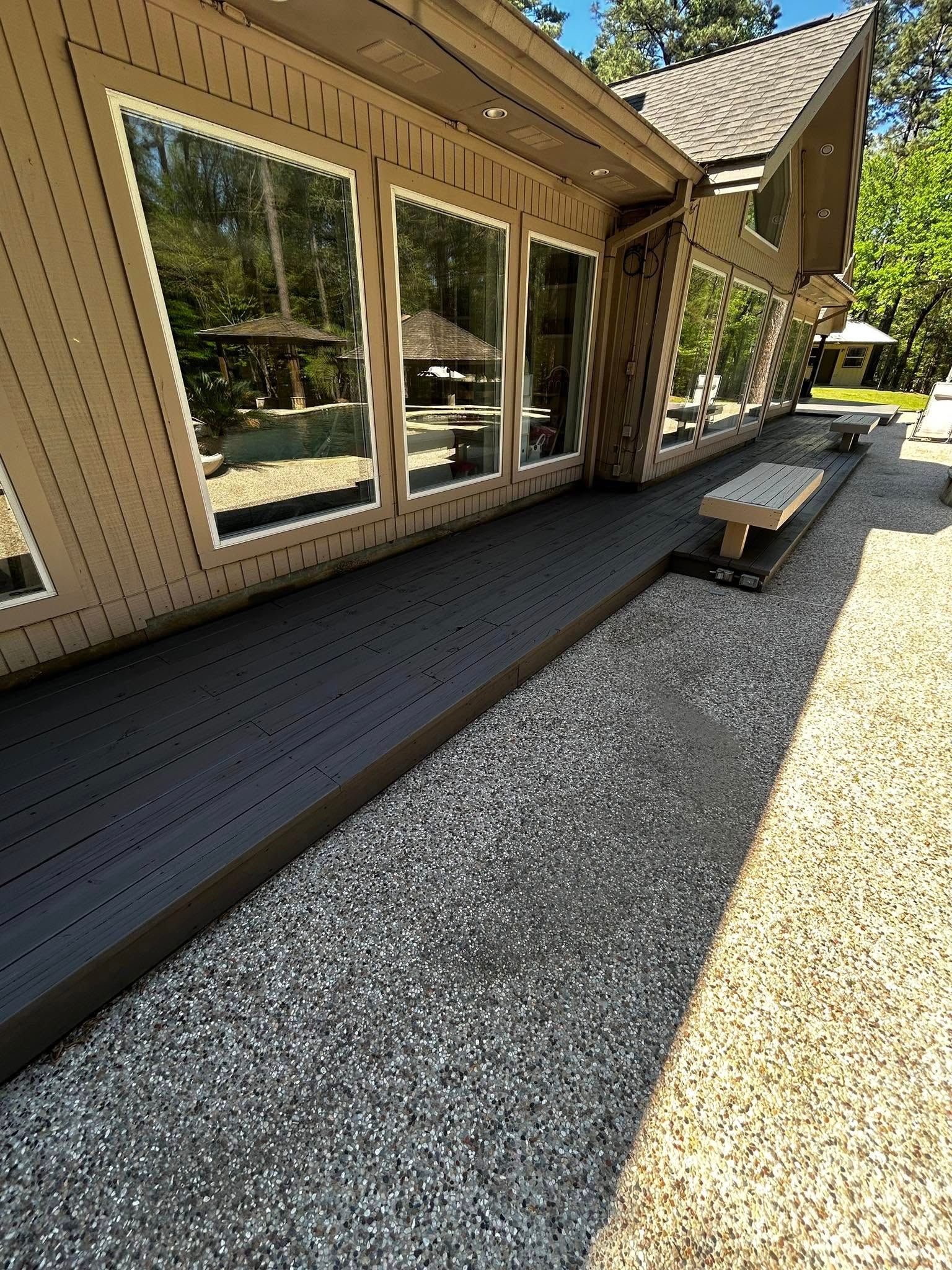 Exterior view of a house with a gravel pathway and a dark gray deck. Large windows reflect trees.
