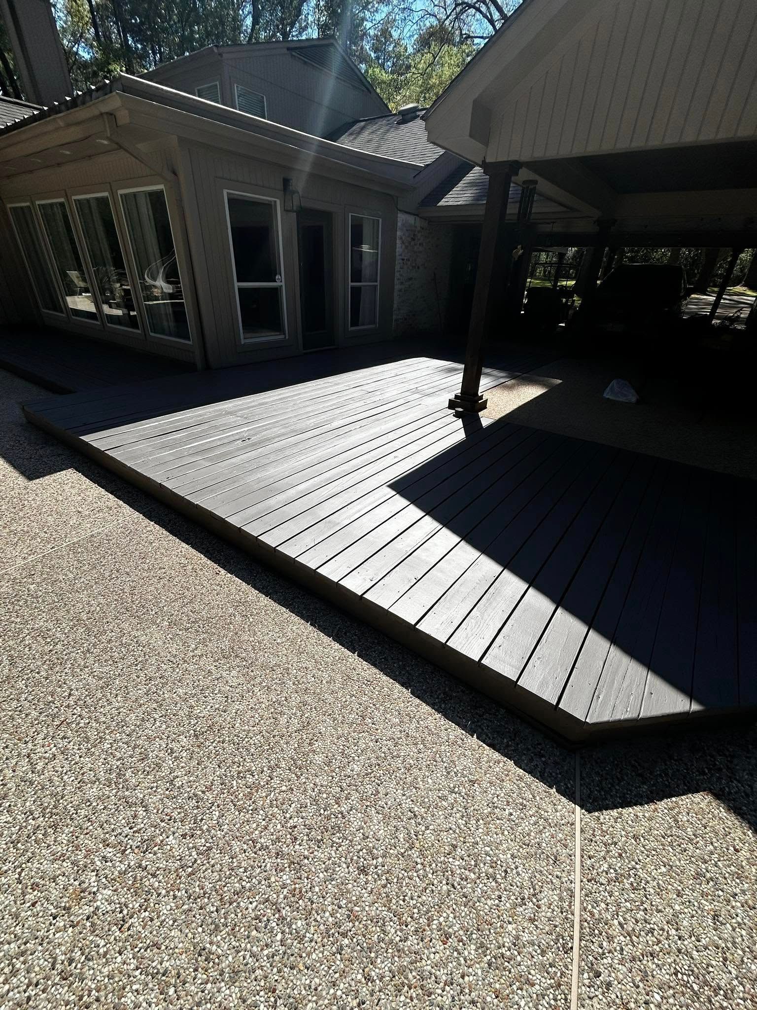 Dark deck next to a speckled concrete patio, adjacent to a home with a shaded area.