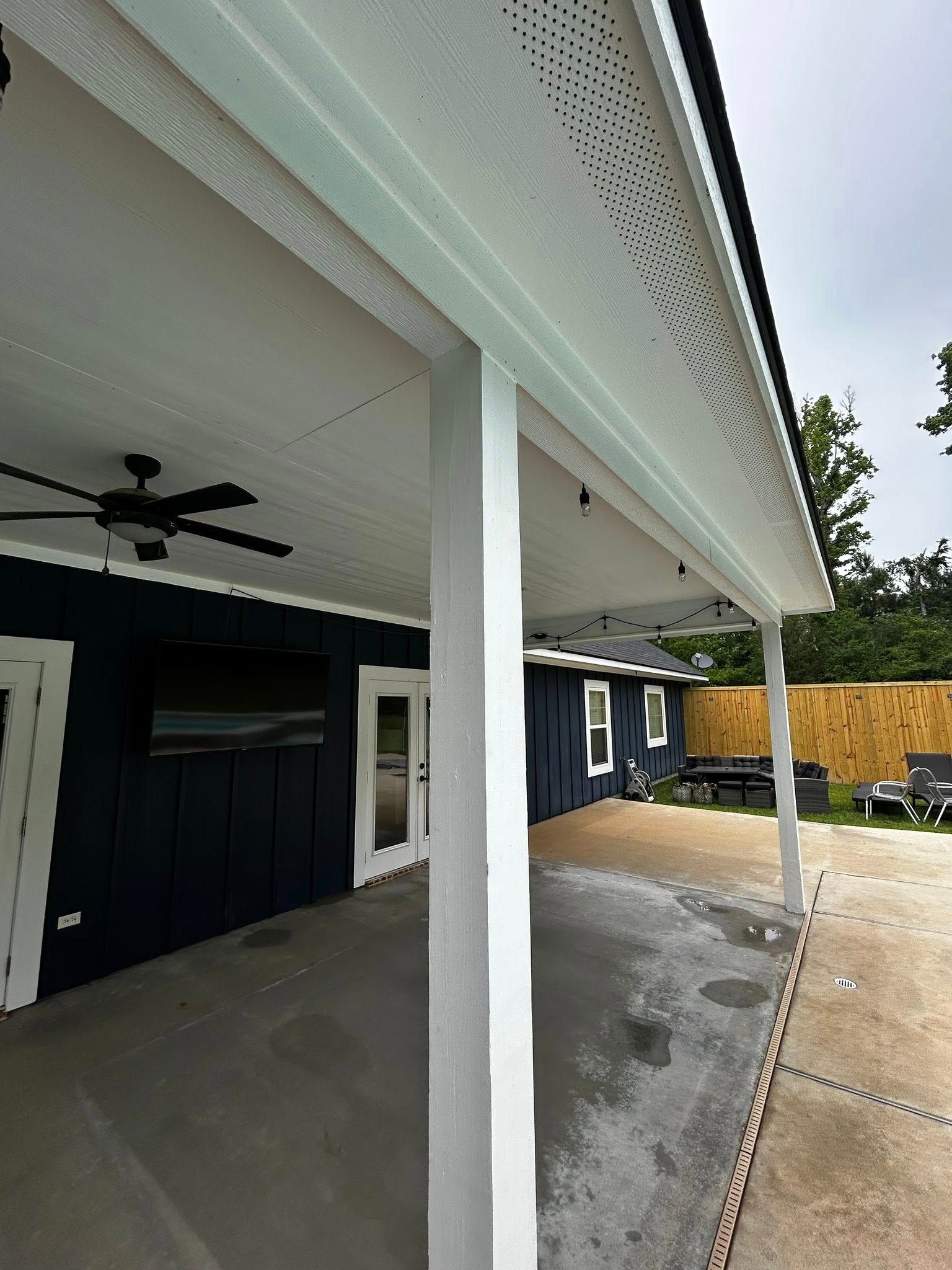 Covered patio with white pillars, blue walls, a TV, and a ceiling fan.
