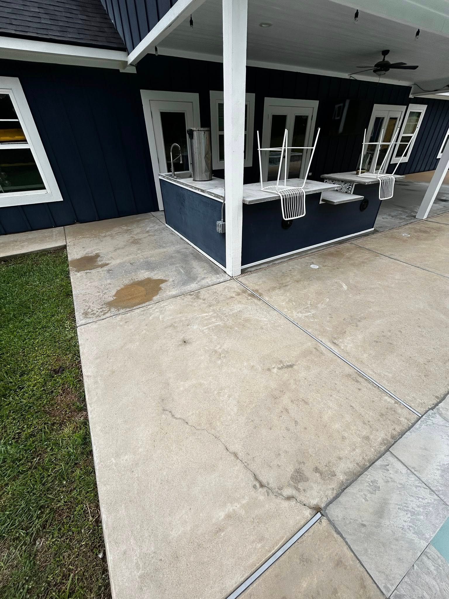 Concrete patio with dark blue house and white trim, covered by a white pergola.
