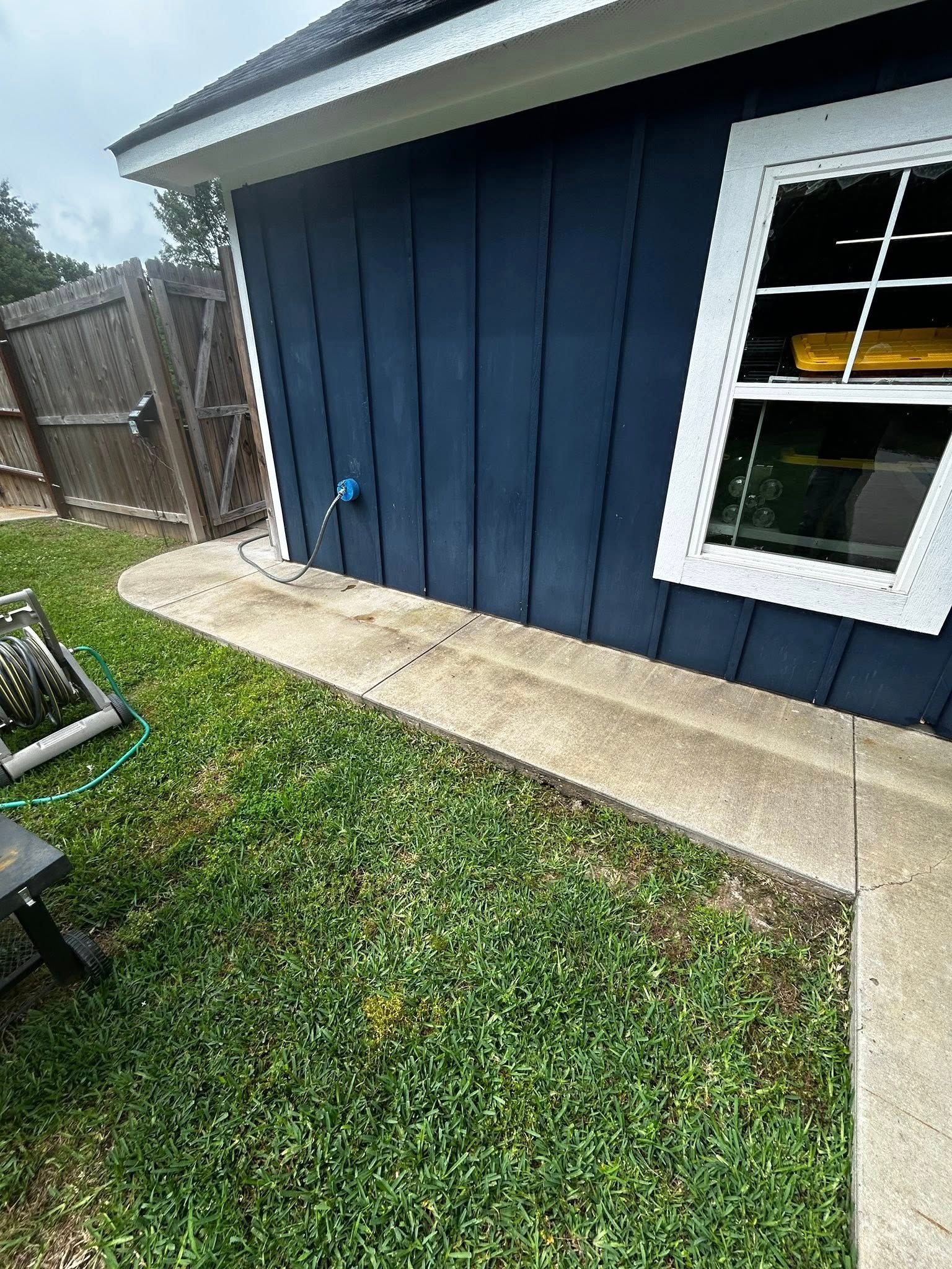Blue building with a white-trimmed window and a concrete walkway bordered by green grass.