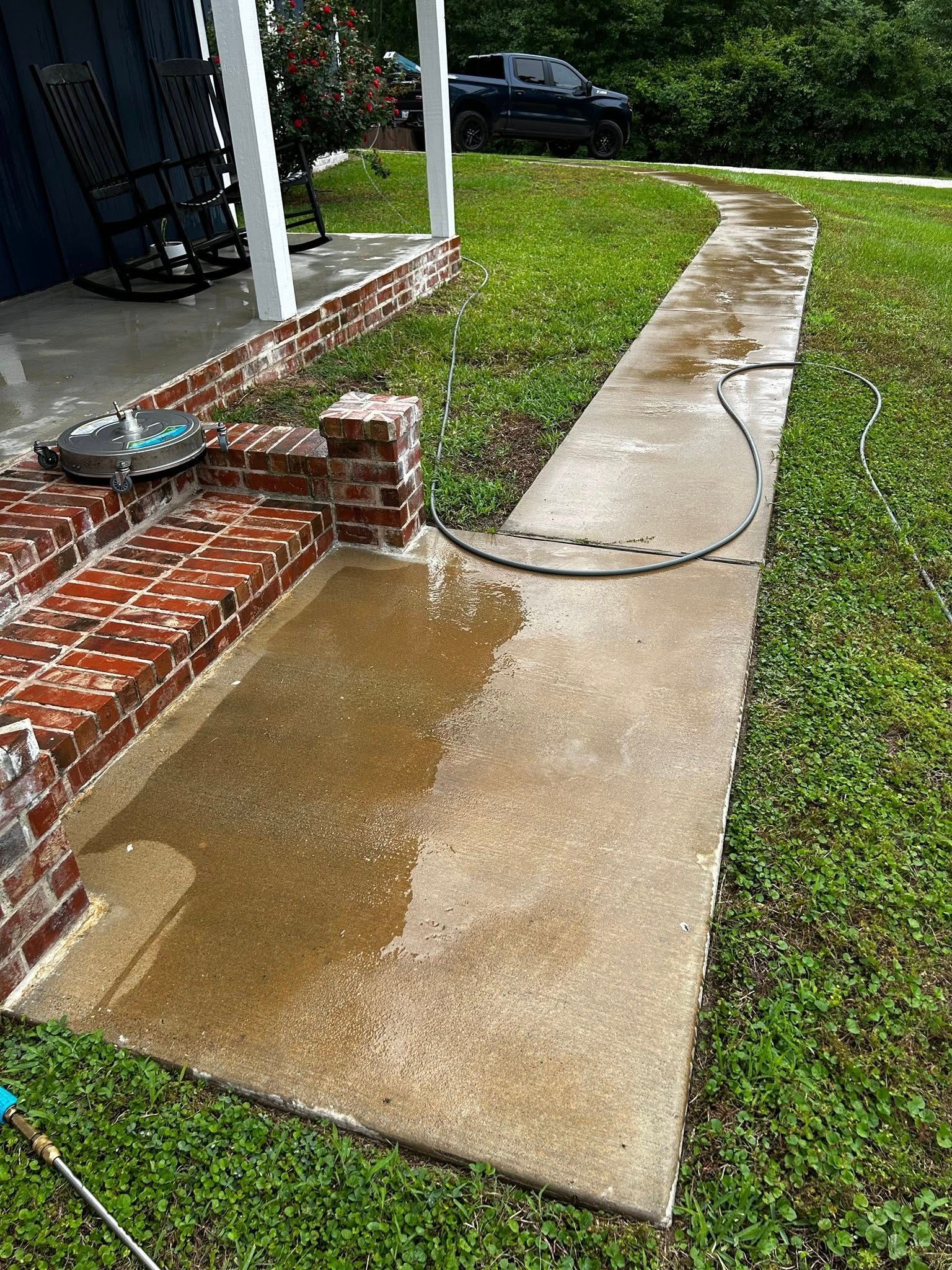 Concrete walkway and porch being power washed, adjacent green grass.