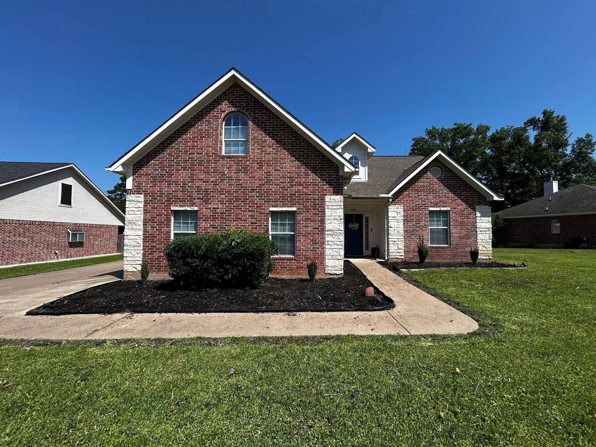 Red brick house with white trim, a blue front door, and a green lawn.