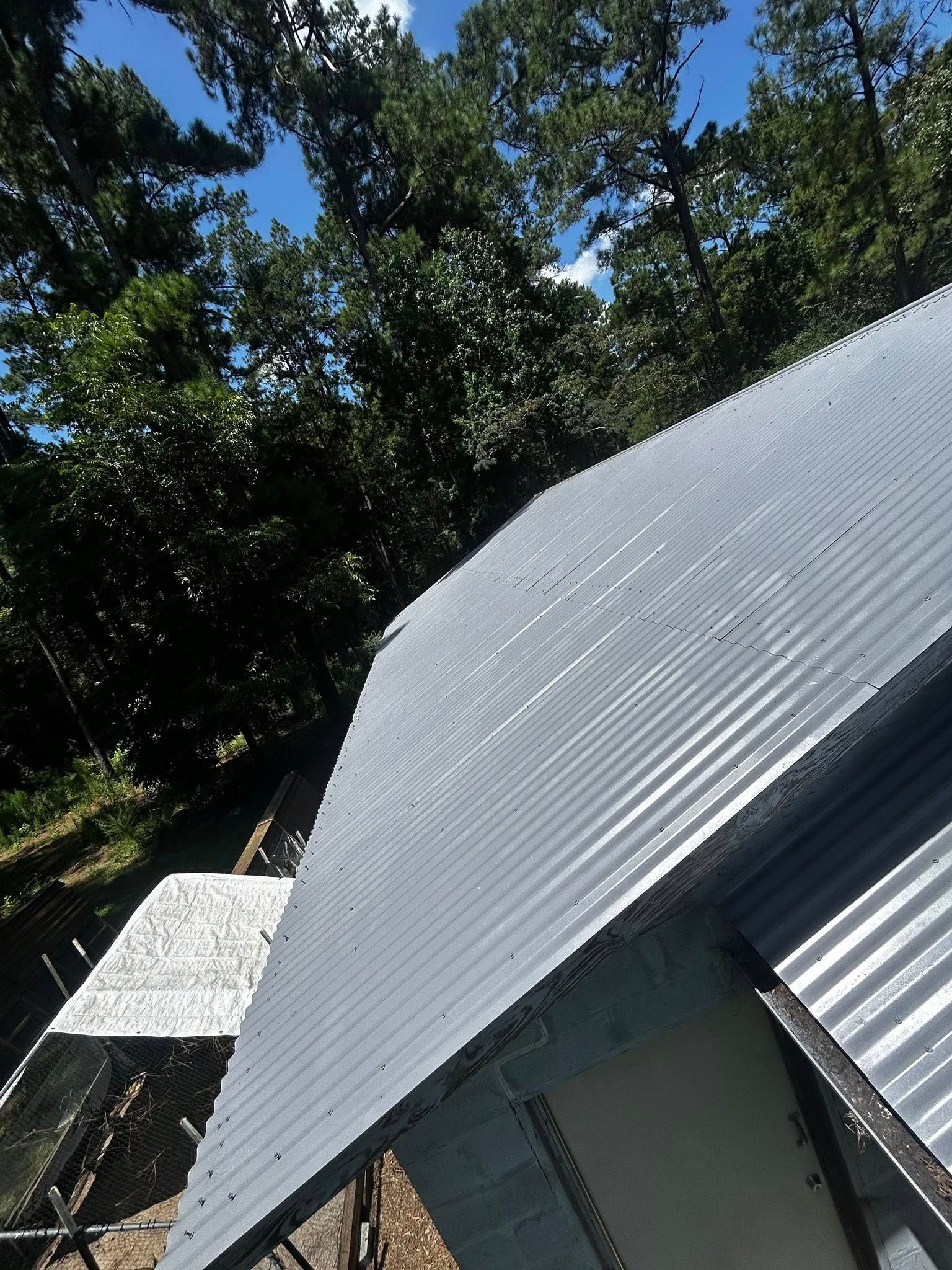 Corrugated metal roof, painted gray, with trees in the background under a blue sky.