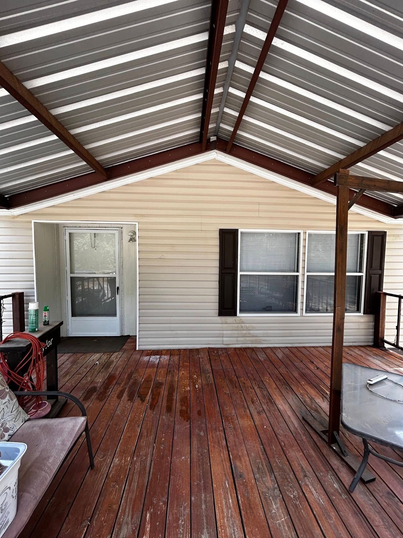 Covered porch of a house with a metal roof. A door and windows are visible. Brown deck and tan siding.