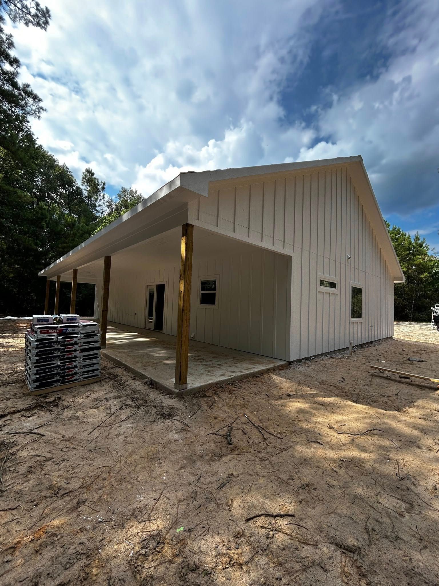 White building with porch, wooden posts, windows, and sand ground under cloudy blue sky.
