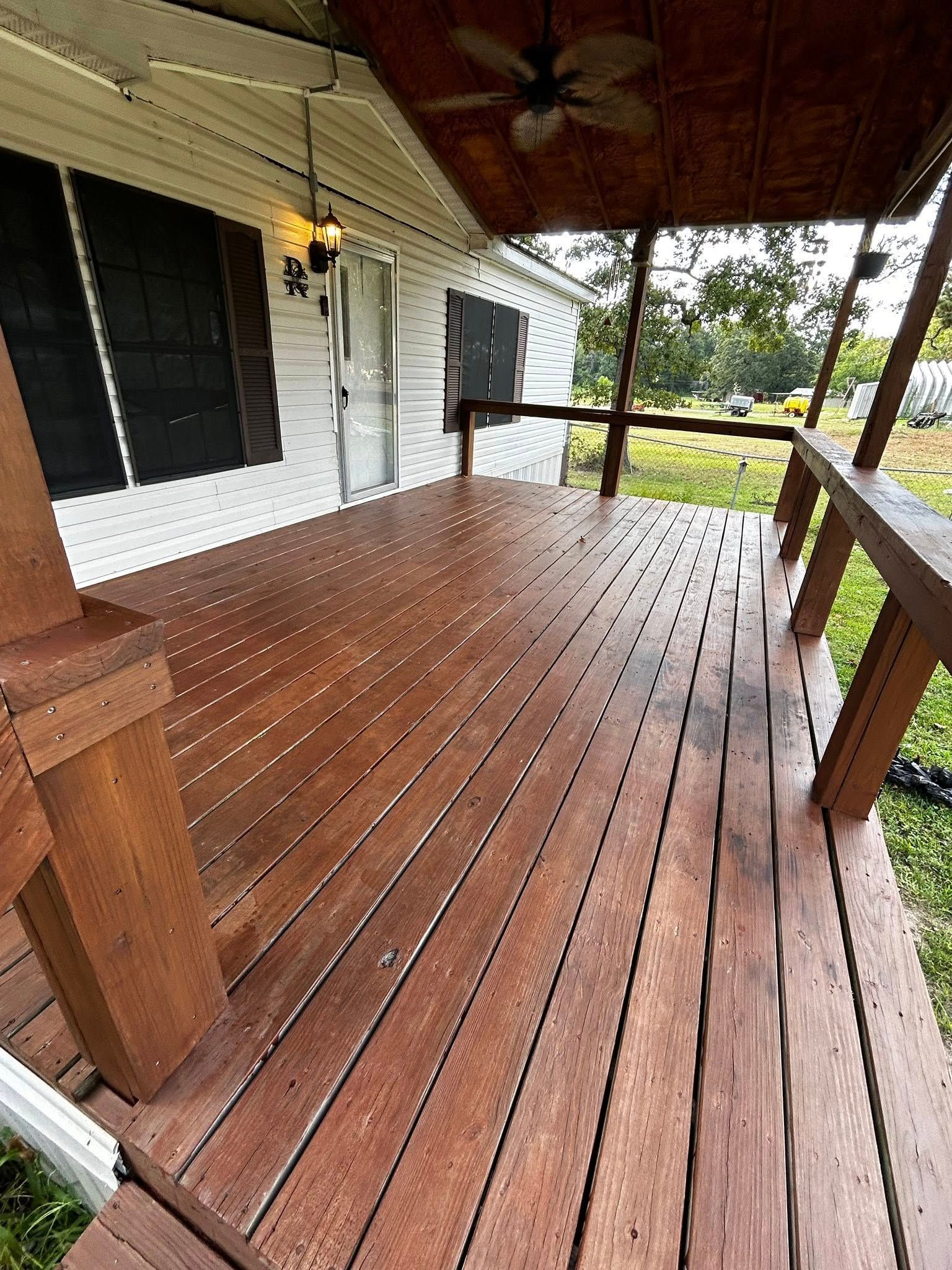 Wooden porch with brown deck, overhead fan, and white siding.