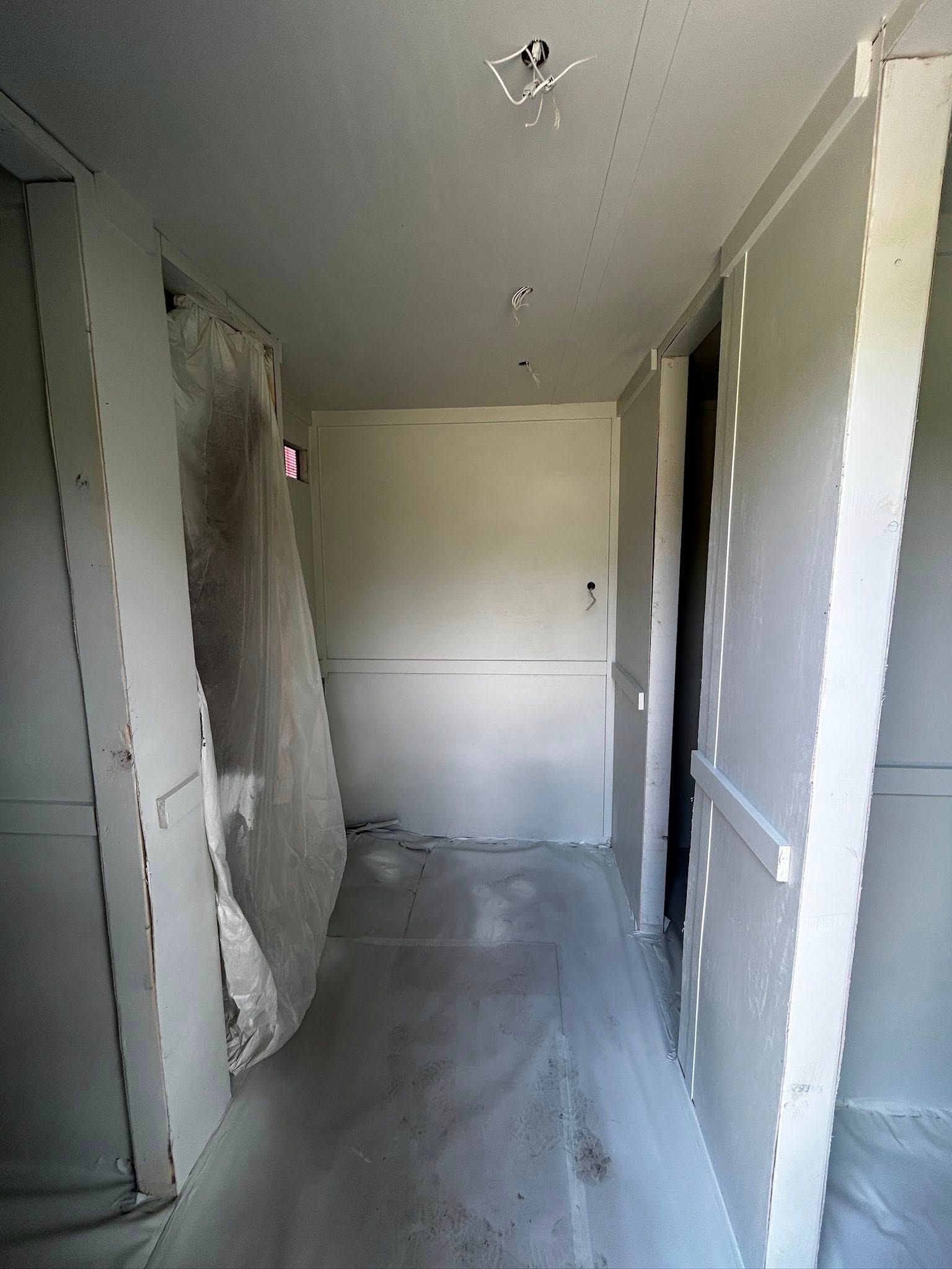 Narrow hallway with drywall under construction; unfinished ceiling and floor, doorway visible.