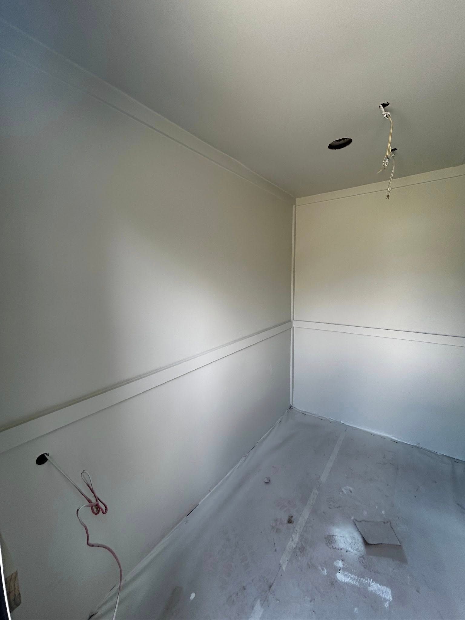 Empty room with light gray walls and concrete floor; electrical wires protrude.