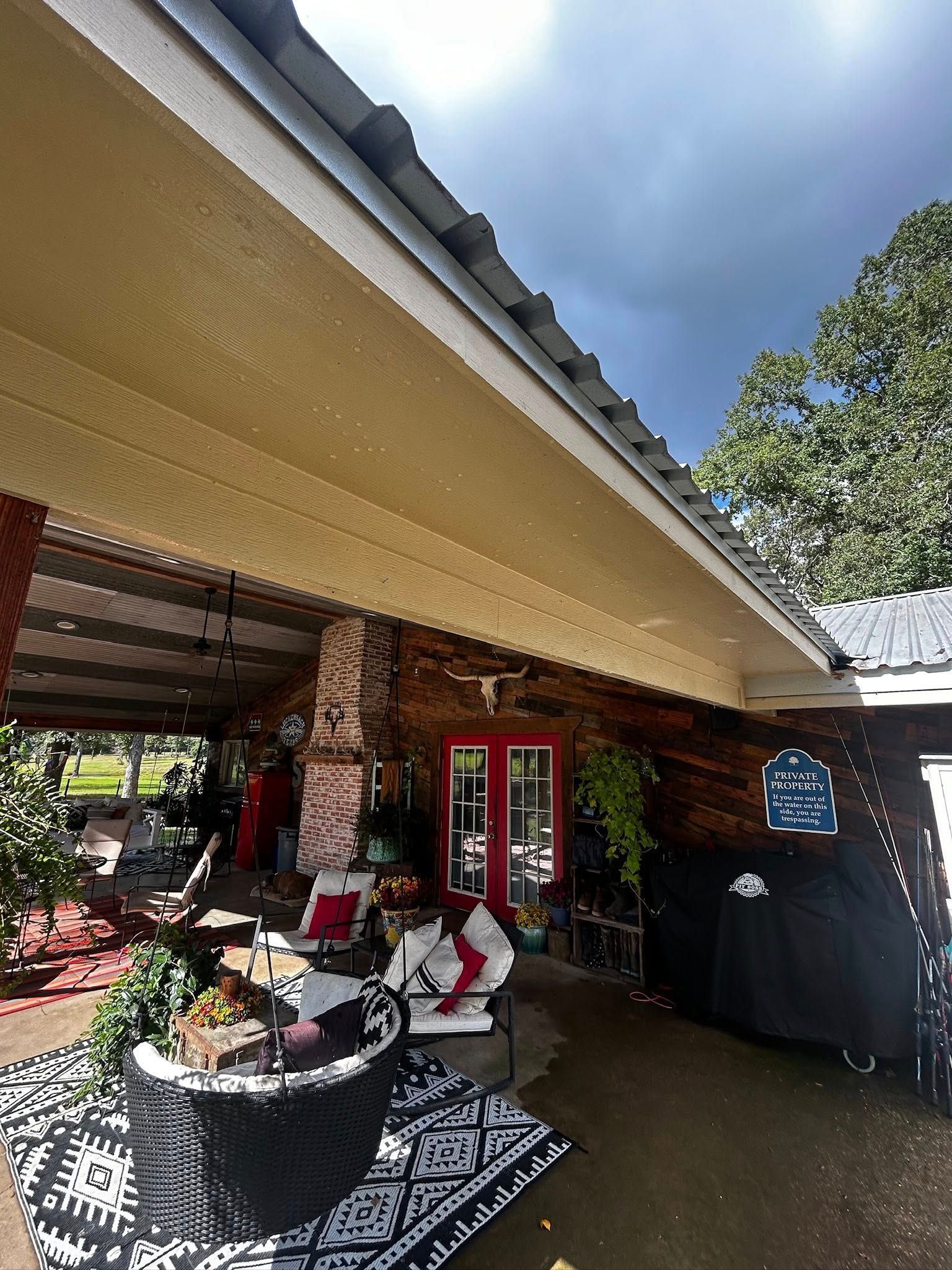 Covered porch with red door, brickwork, seating, and plants. Cloudy sky overhead.