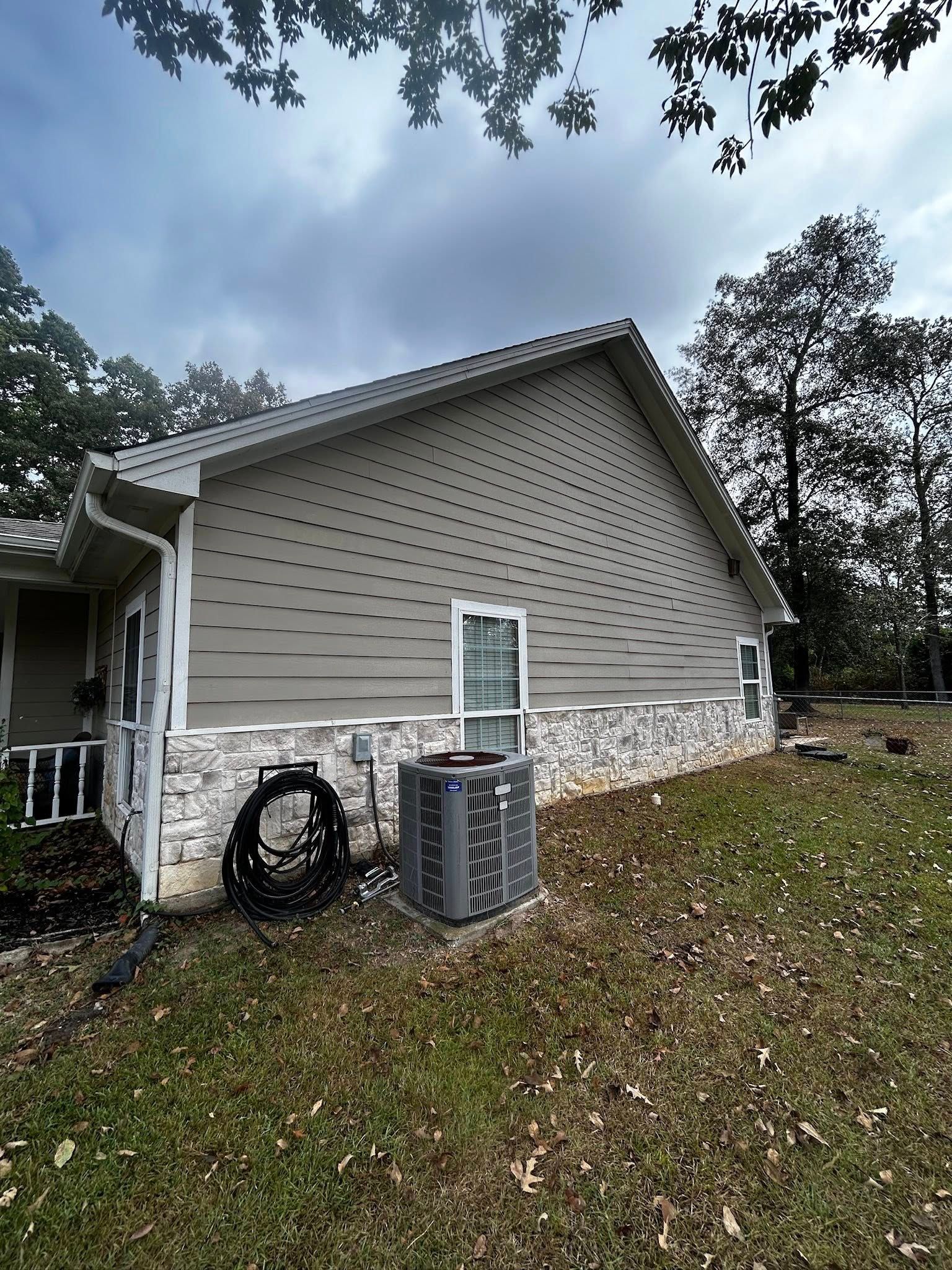 A house with beige siding and stone foundation, with an air conditioner unit and overcast sky.
