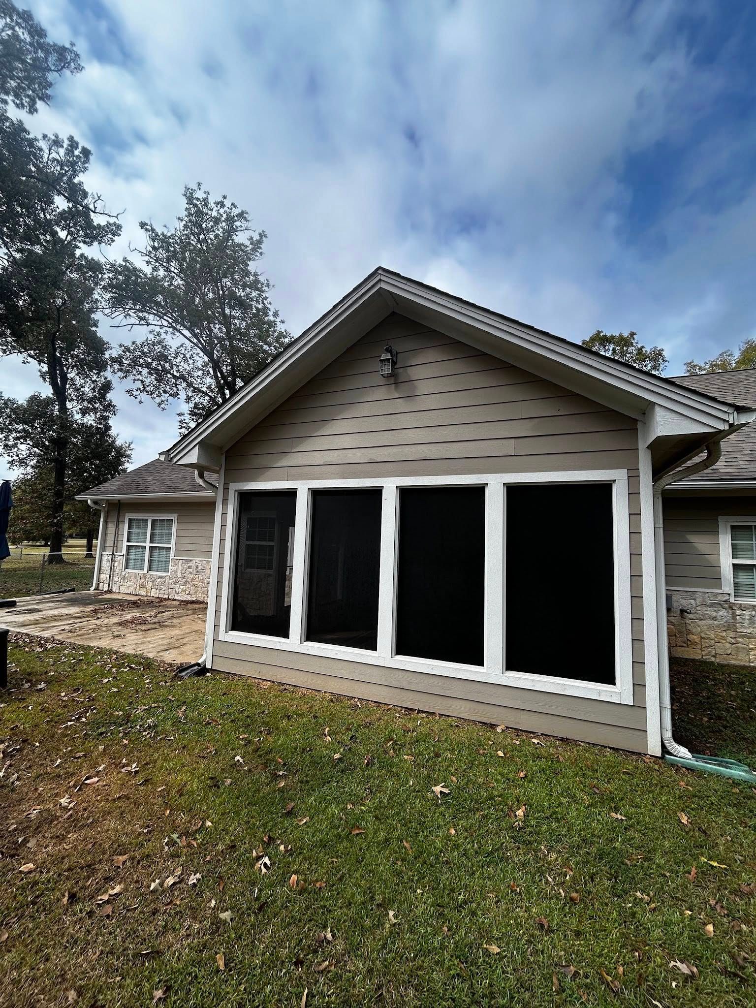 Tan-sided house with screened porch, white trim, and a lawn under a cloudy sky.