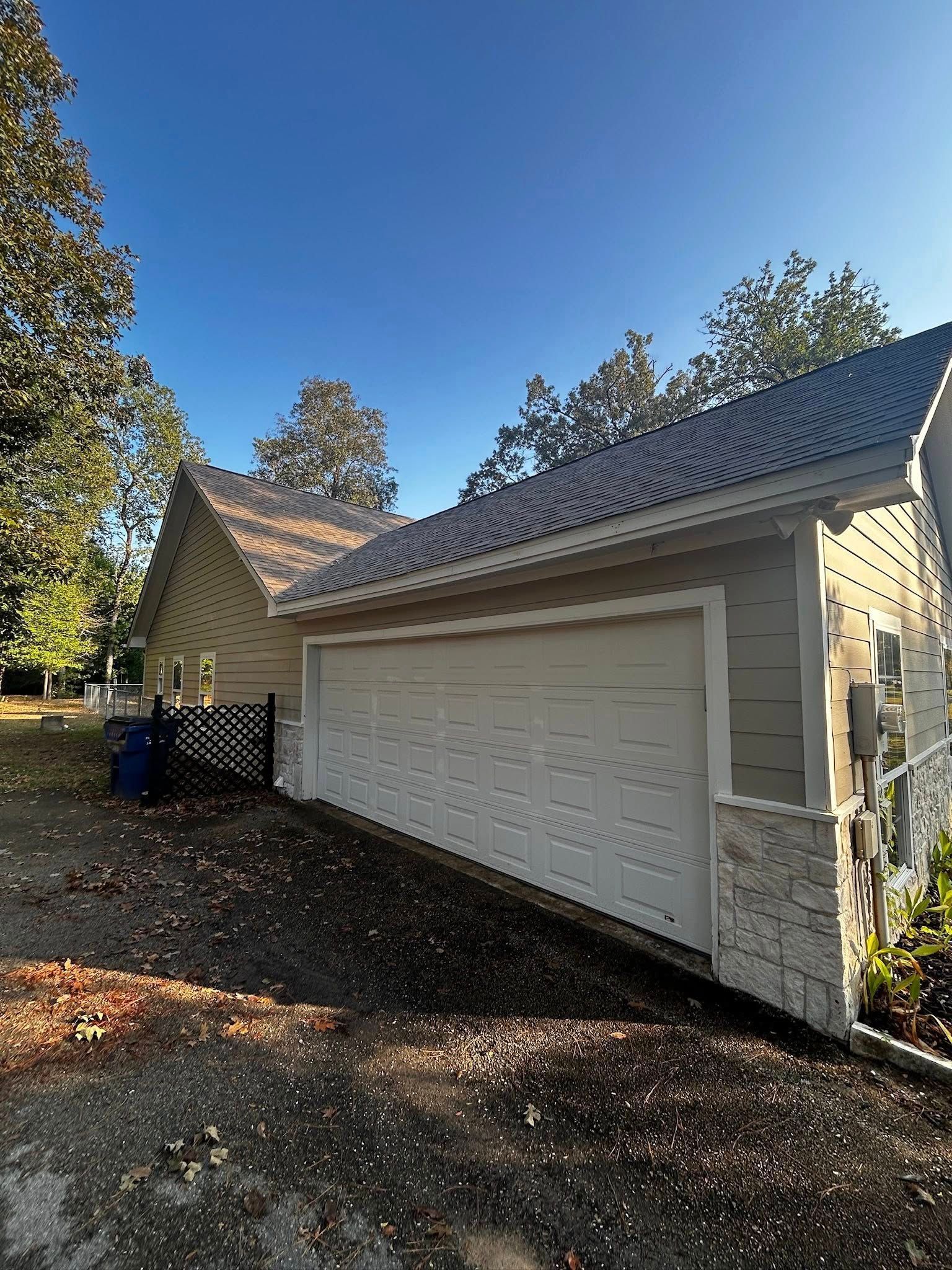 Garage with a white door, light-colored siding, and a tile roof against a blue sky.