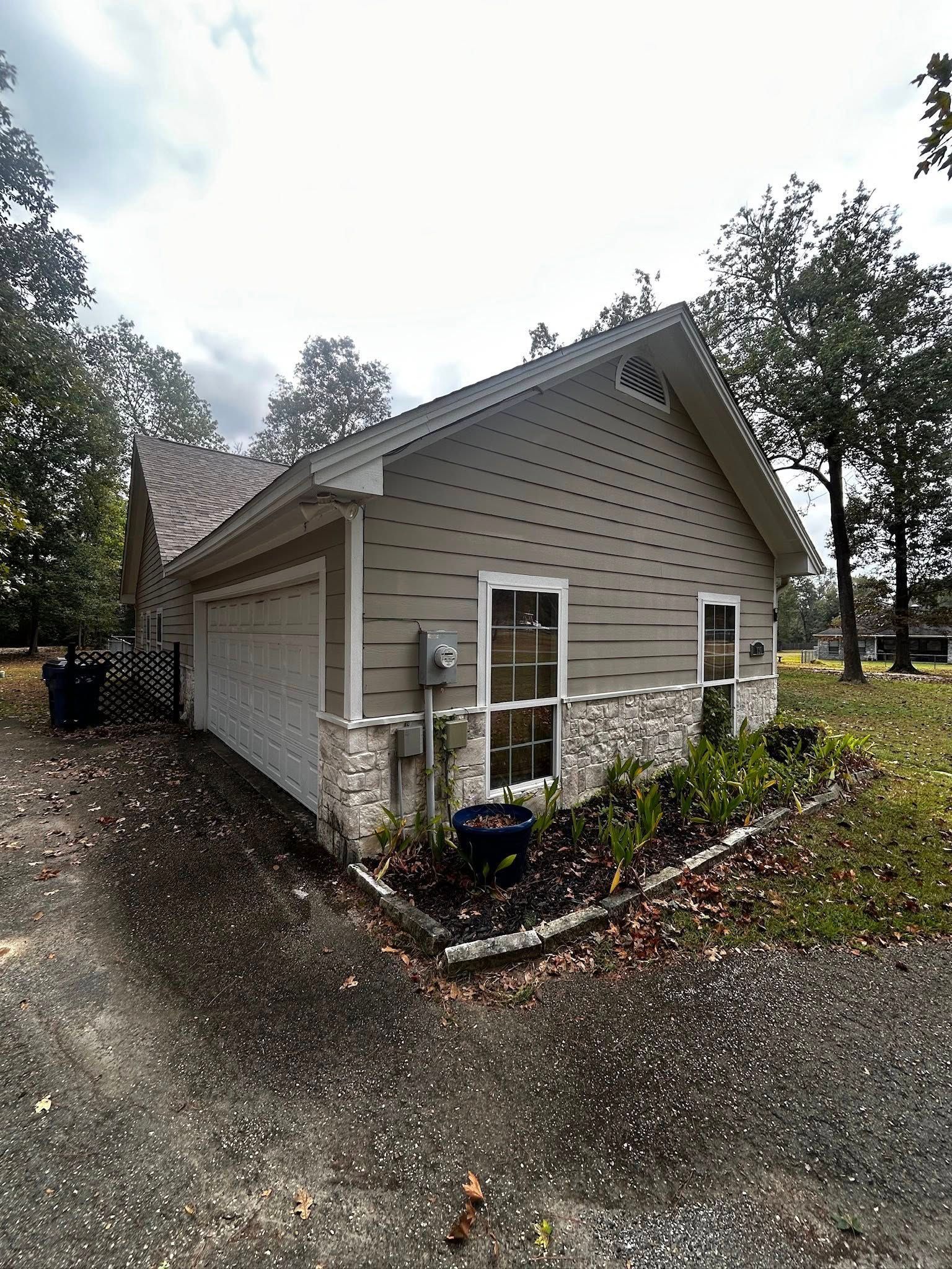 Tan house with stone foundation, small windows, and a driveway. Trees in background.