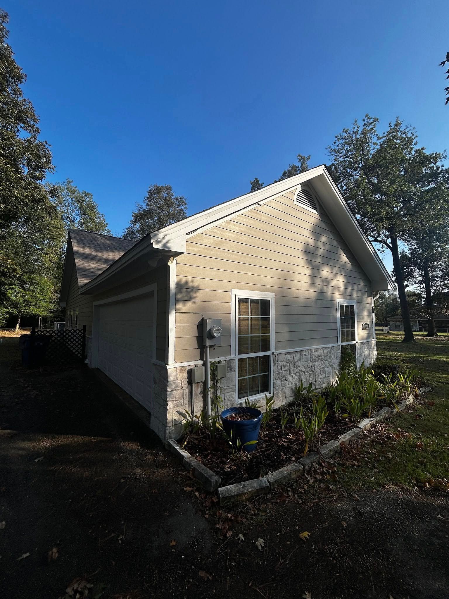Side view of a light gray house with a small garden in front, under a clear blue sky.