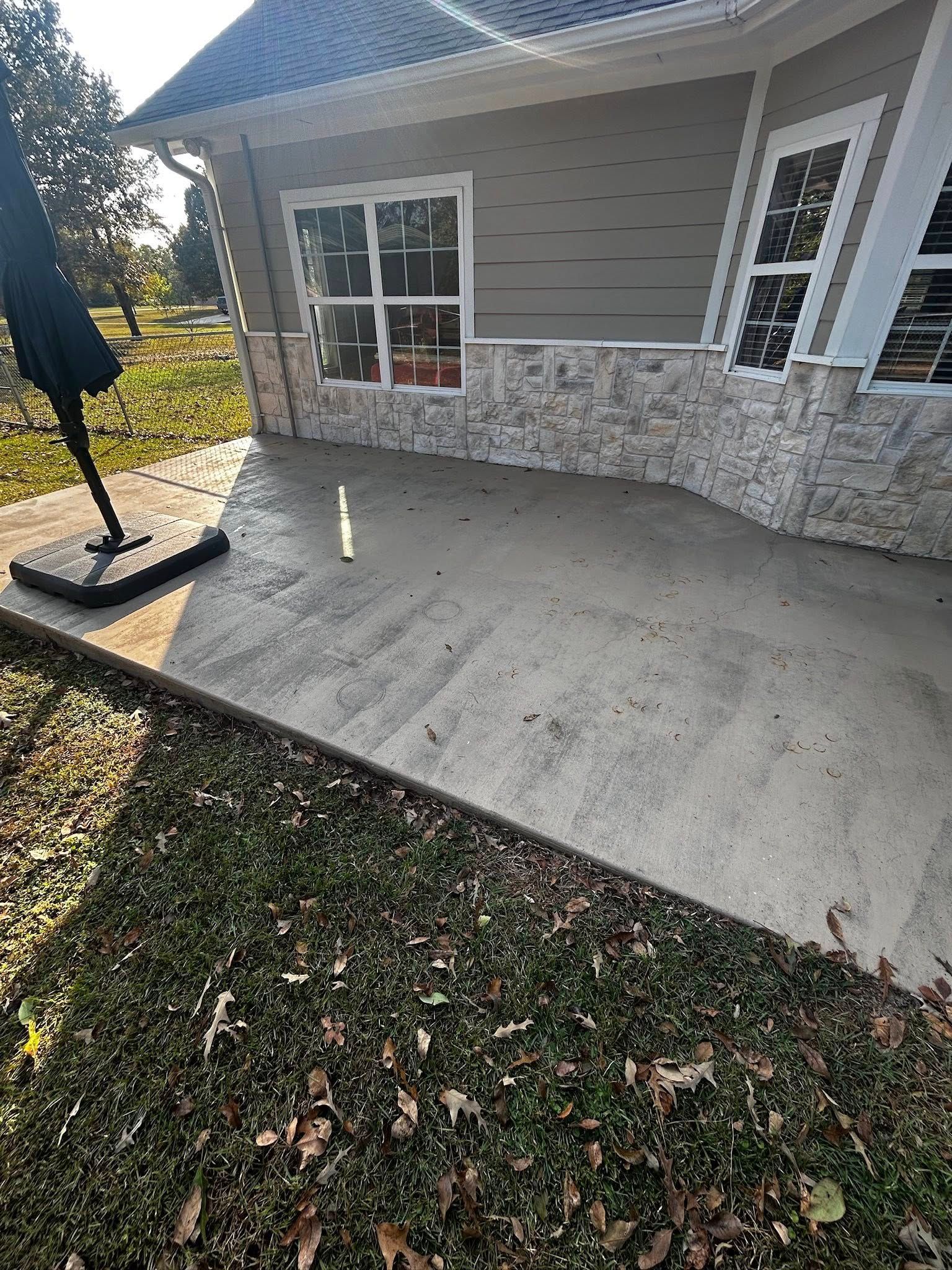 Concrete patio in front of a house, with grass border and umbrella.