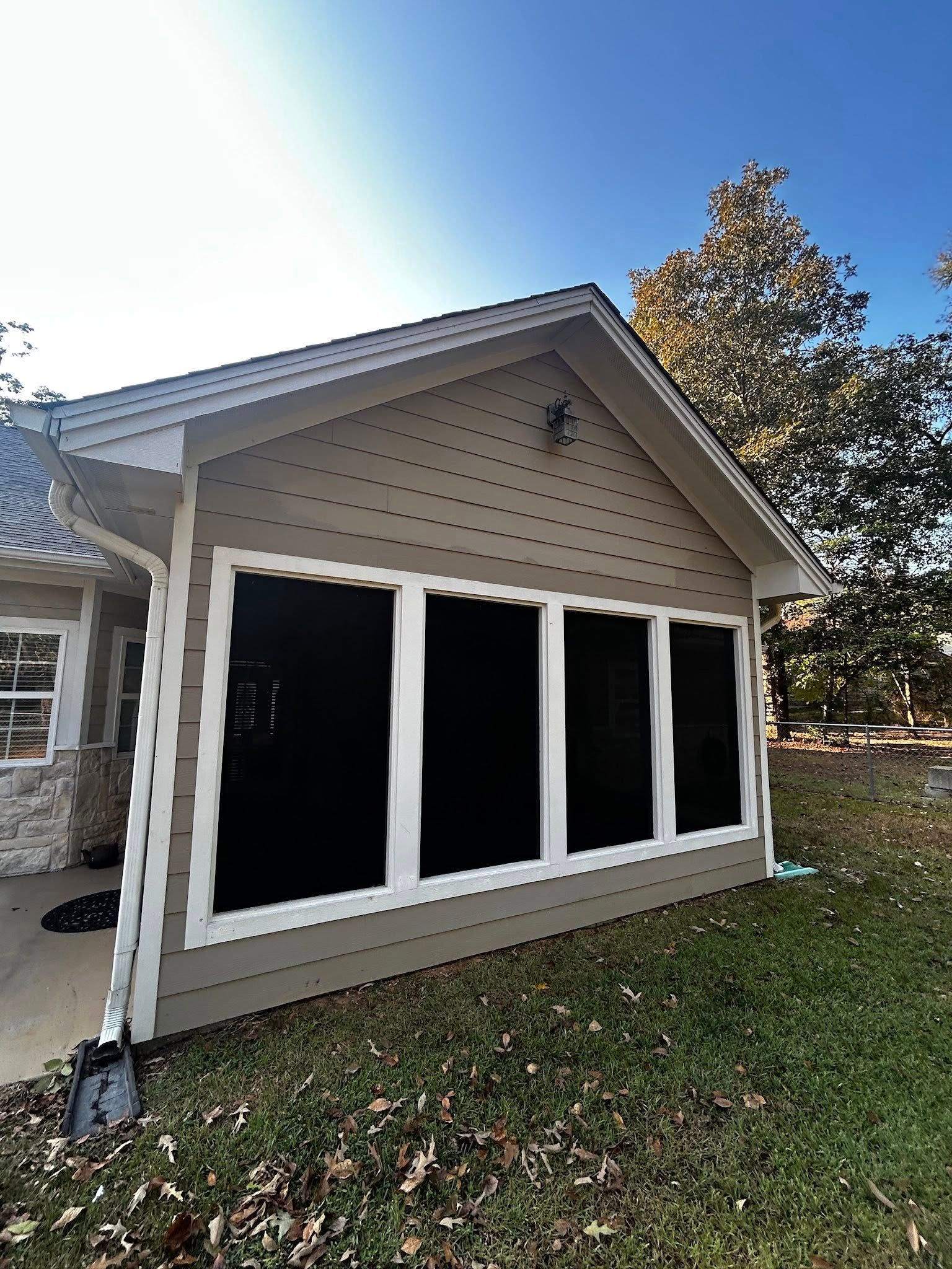Tan-sided house addition with large black-screened windows under a blue sky, on a grassy lawn.