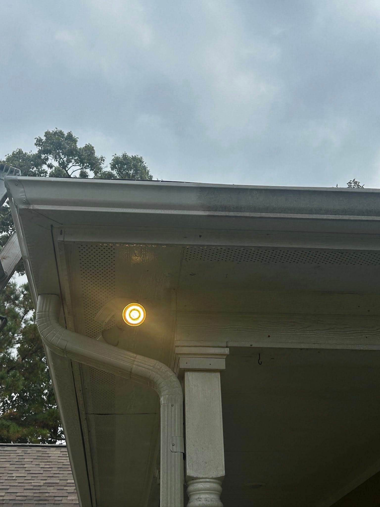 A glowing outdoor light fixture on a house's corner, under a gray sky.