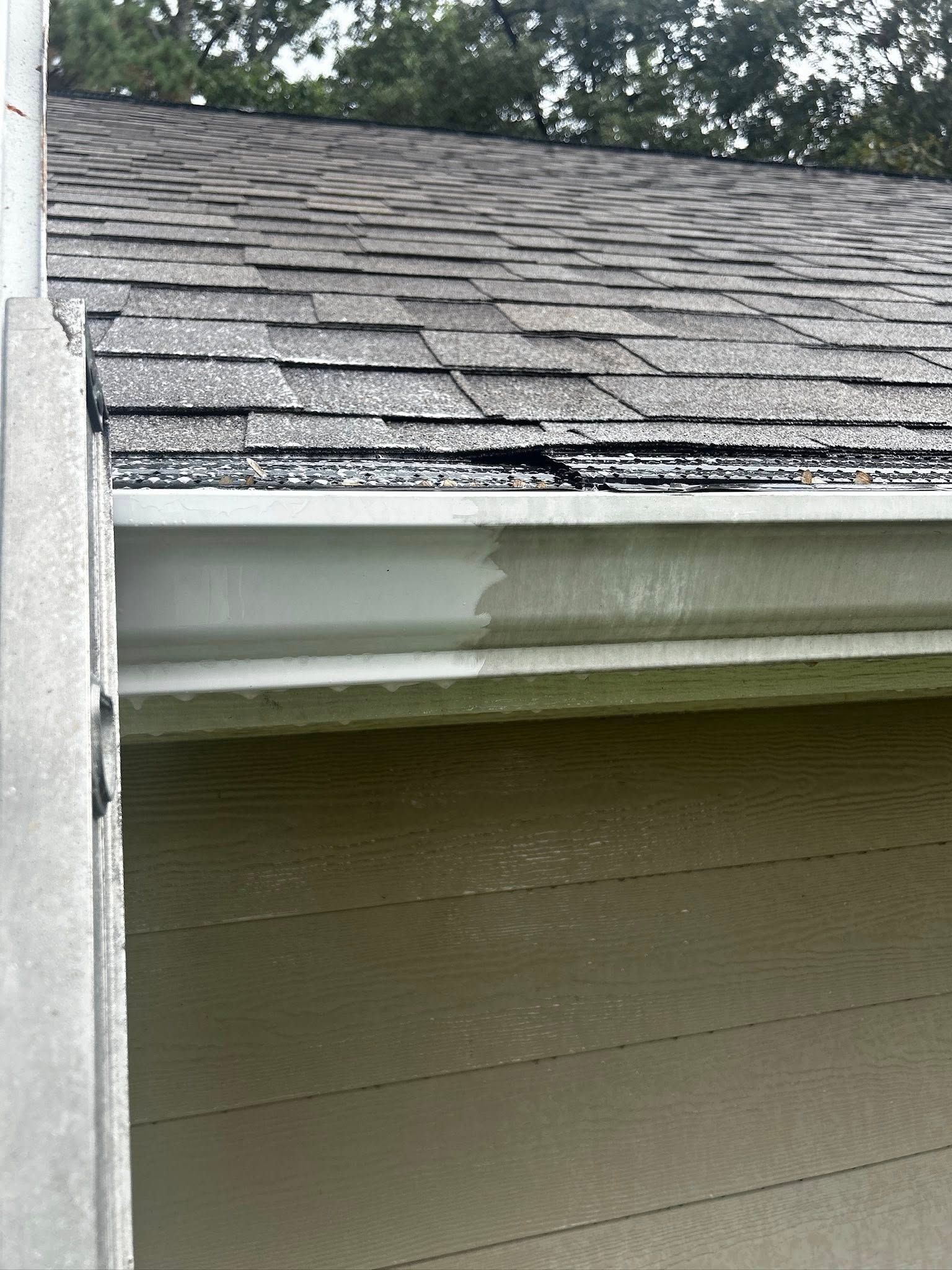 A close-up of a house gutter that is filled with debris and dark spots, partially cleaned.