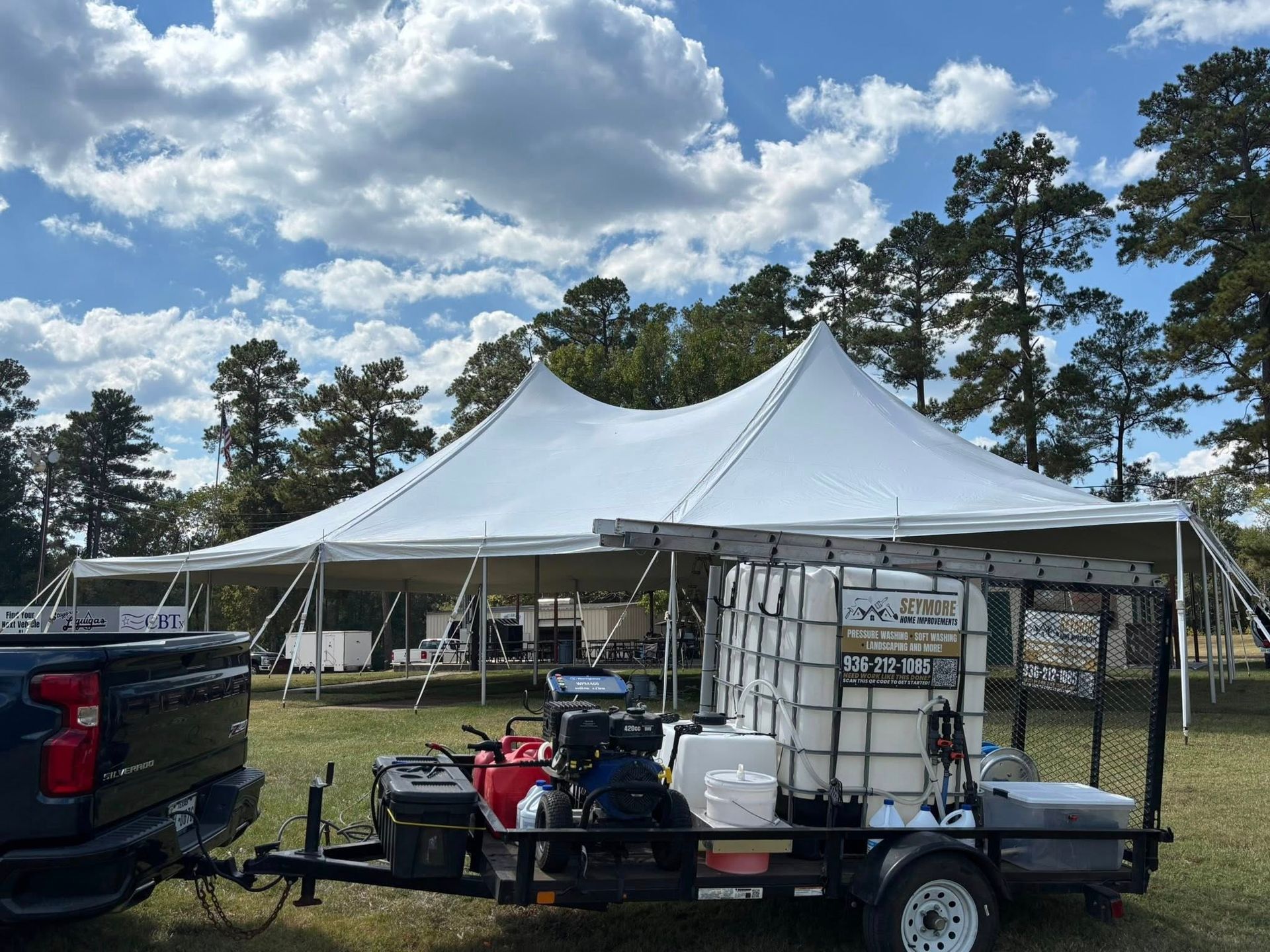 A white tent set up in a grassy field, with a trailer holding equipment in front of it.