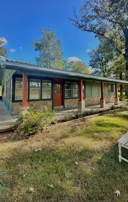 Green house with stone and wood accents under a blue sky, porch with columns.
