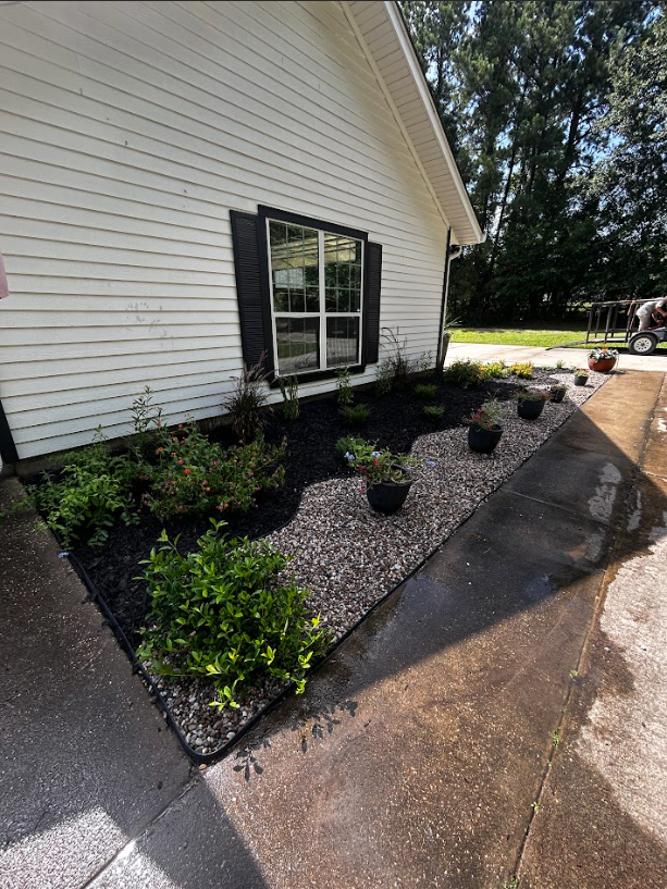 Garden bed with black mulch and gravel next to a white house with black shutters.