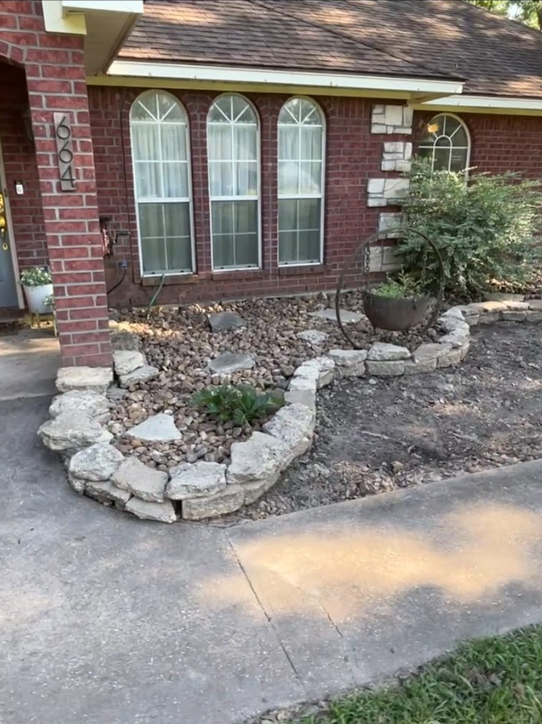 Brick house with stone-edged flower bed, arched windows, and concrete walkway.