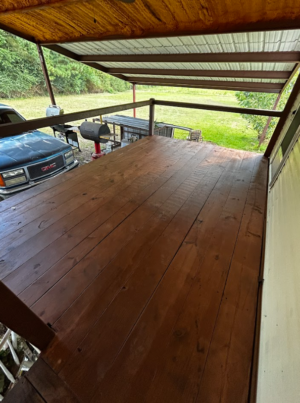 Wooden deck under a metal roof, overlooking a grassy yard with a truck and grill.
