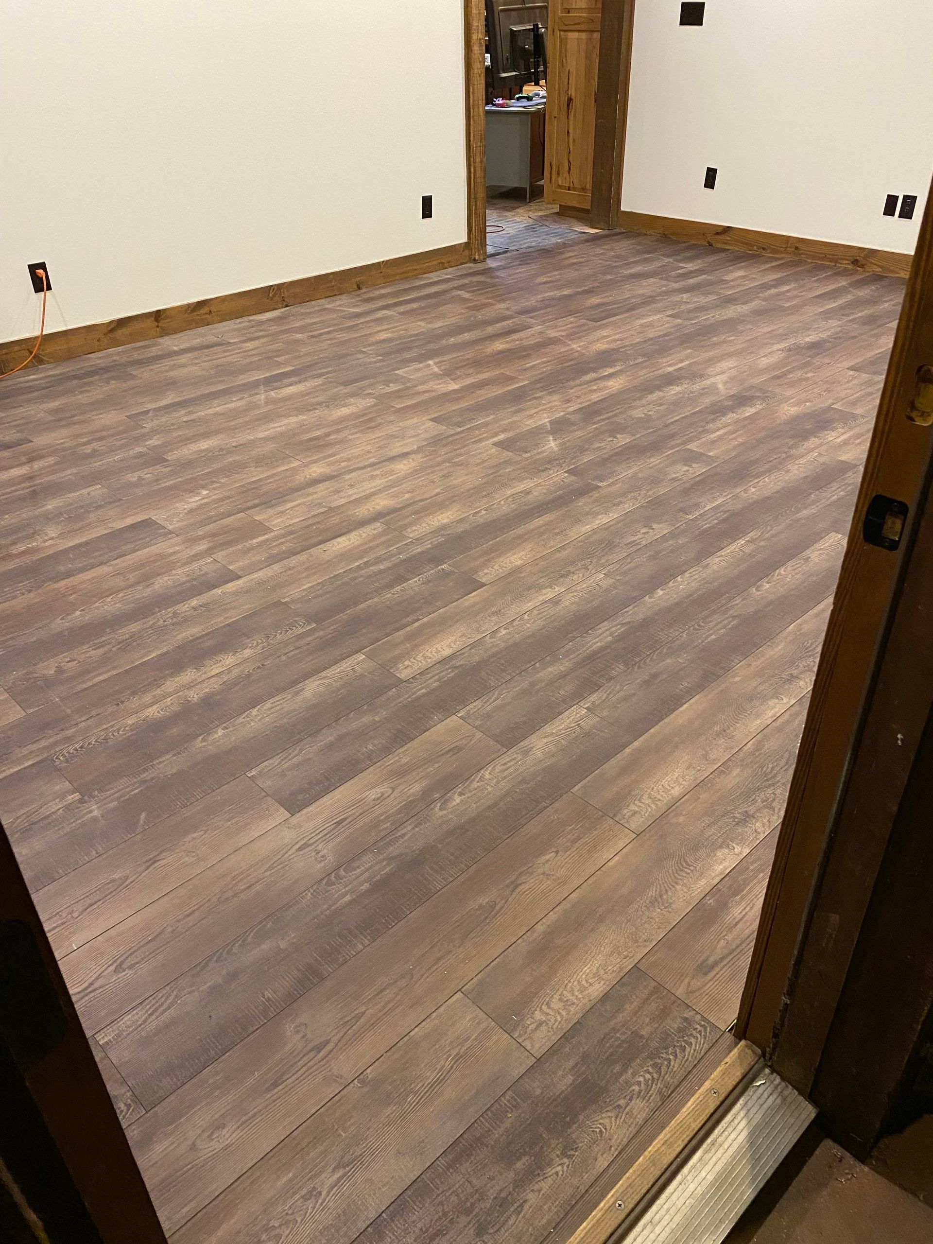 Room with wood-look flooring and trim, white walls. Doorway in the foreground, another in the background.