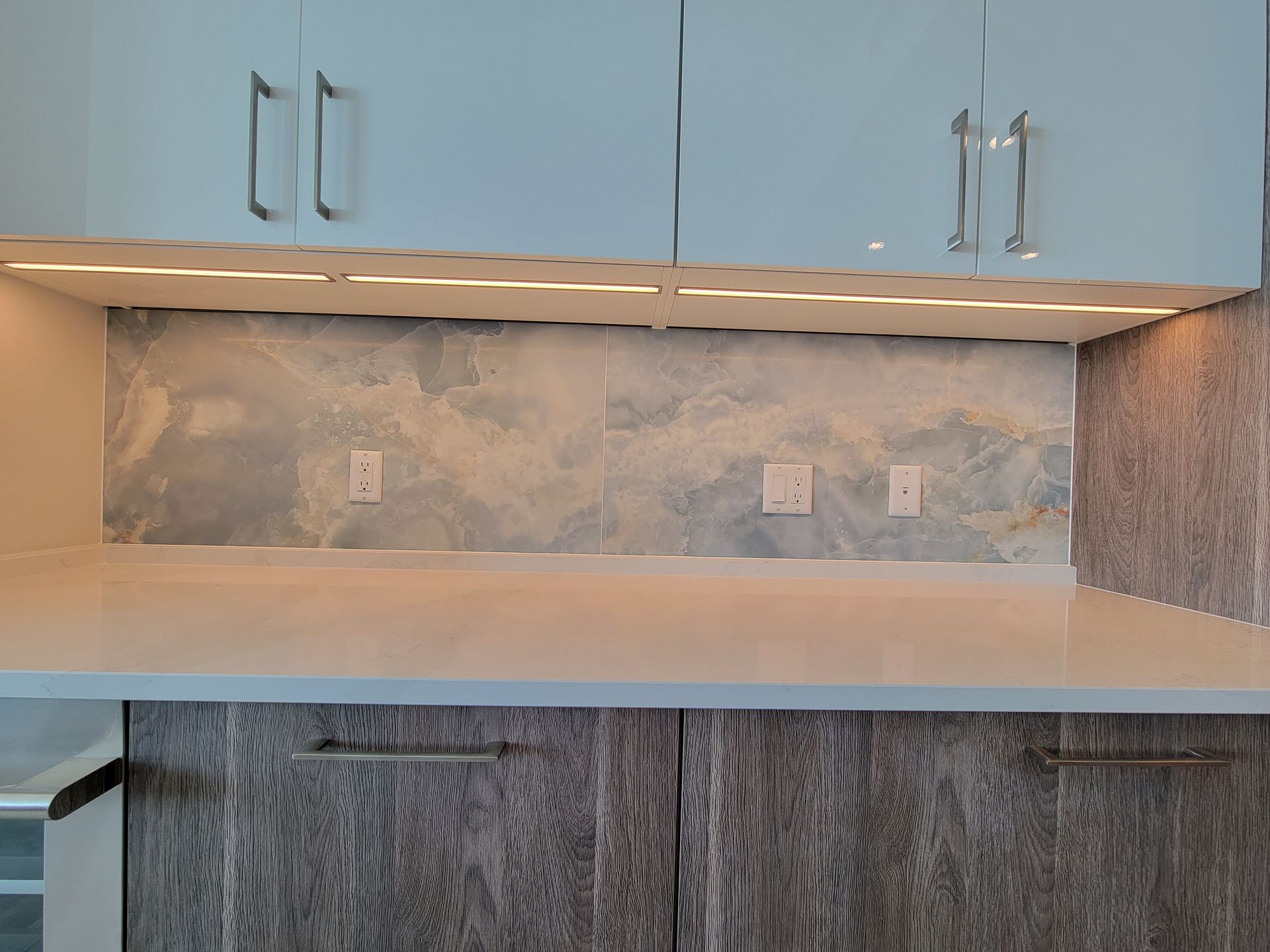 Kitchen with light blue marble backsplash, white countertops, and gray cabinets.