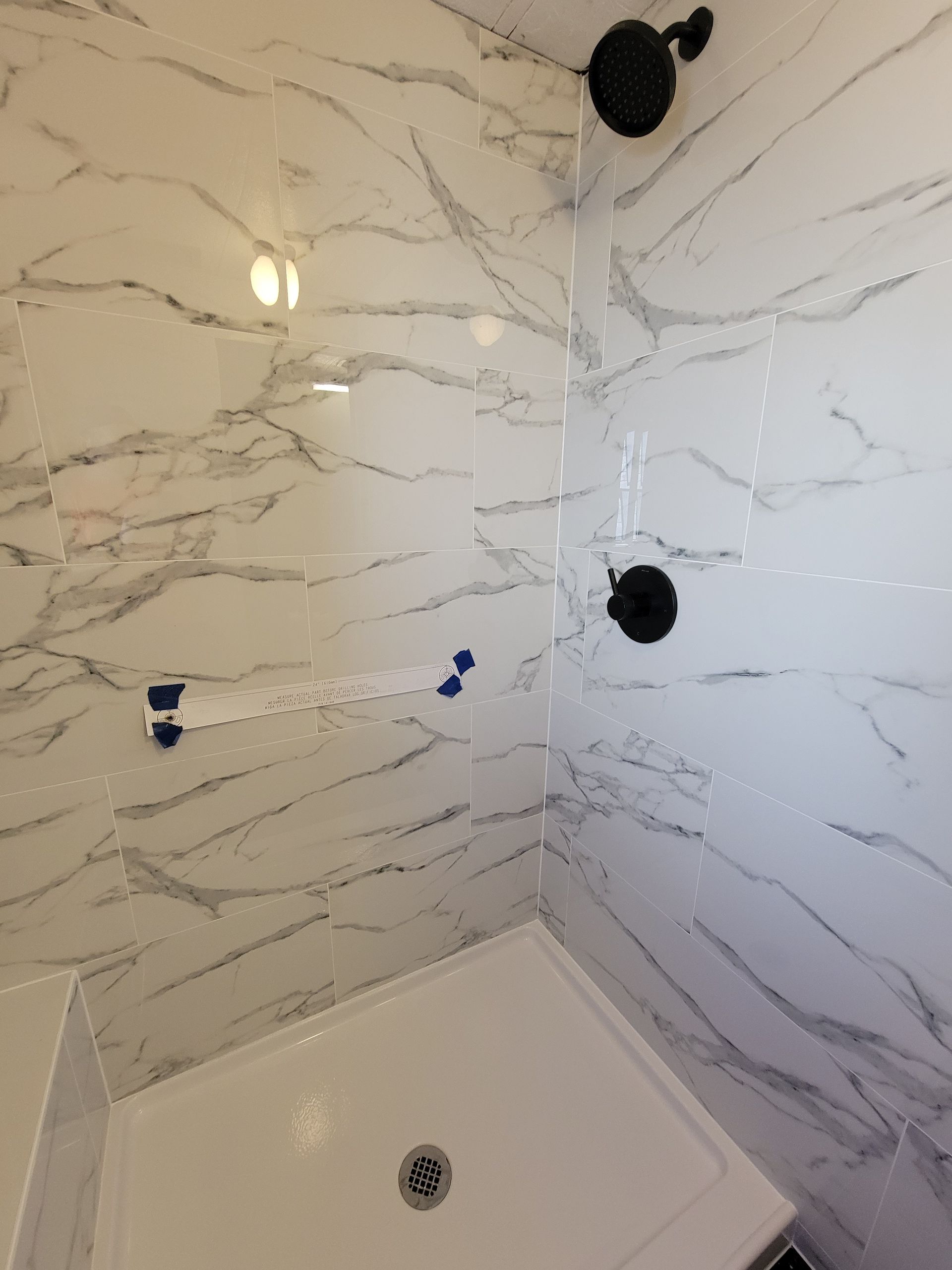 White marble-tiled shower with black fixtures and a white shower base.
