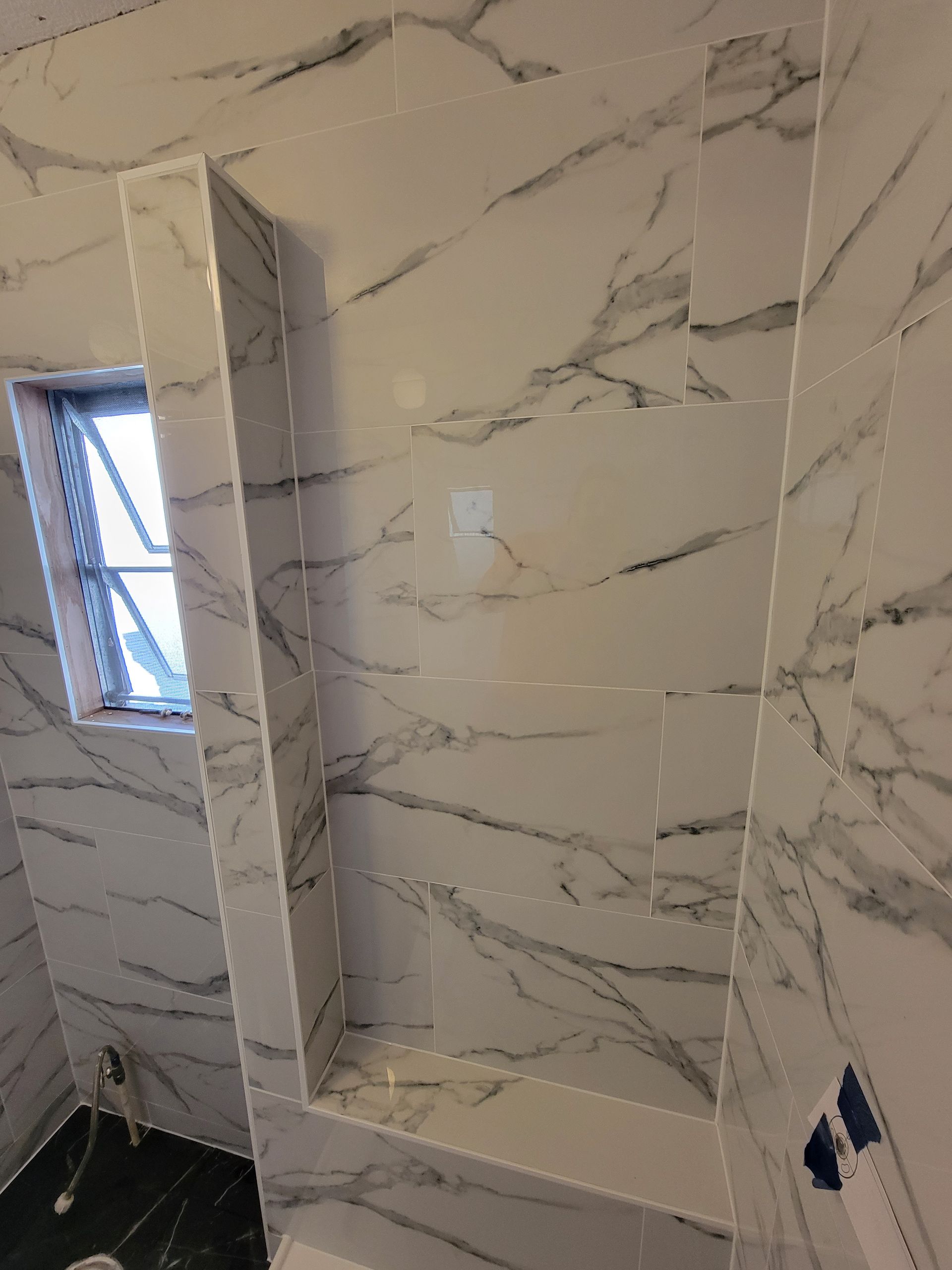 White marble-look tiled shower with recessed shelf and small window.
