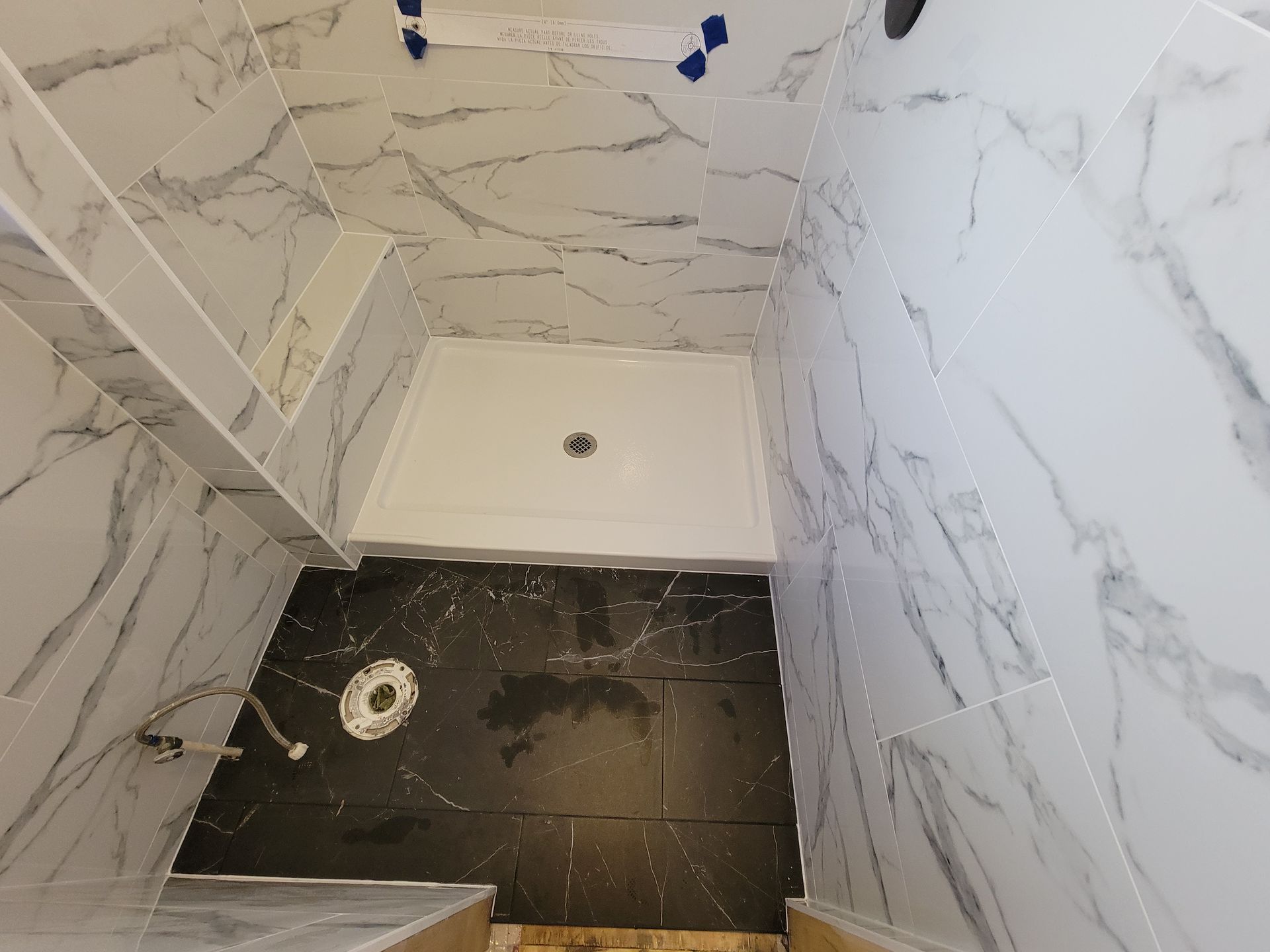 Bathroom with marble-patterned white tiles, black floor tiles, and a white shower basin.