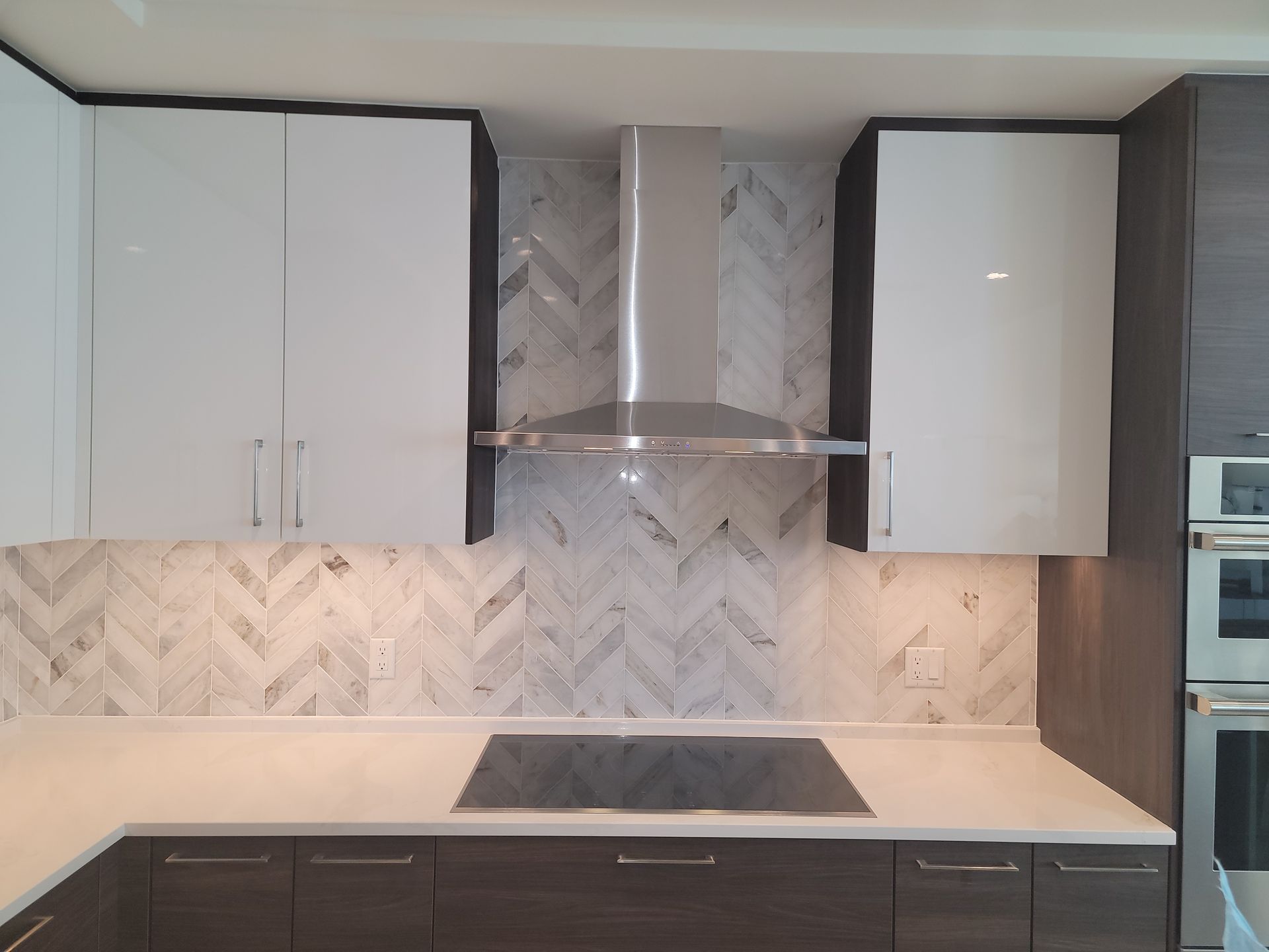 Modern kitchen with white and dark cabinets, backsplash, range hood, and stovetop.