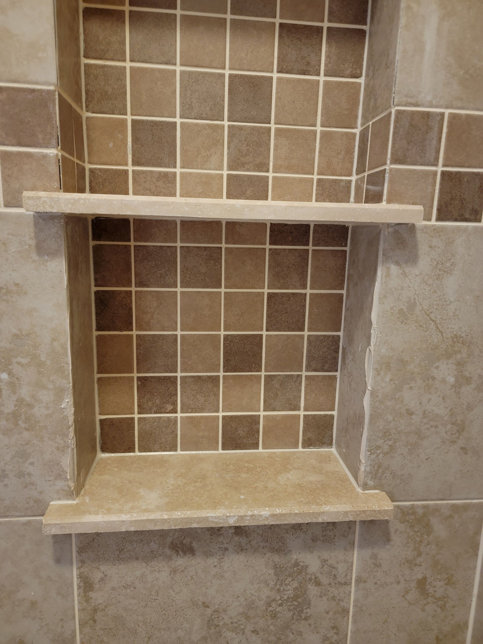 Bathroom shower niche with two shelves, tiled interior, beige and brown tones.