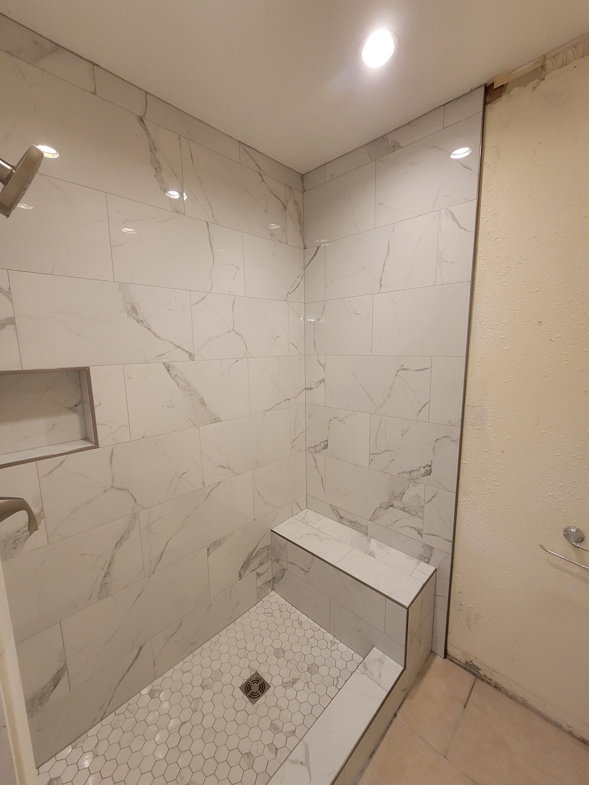 Shower stall with marble-look tiles, a built-in bench, and a recessed shelf.