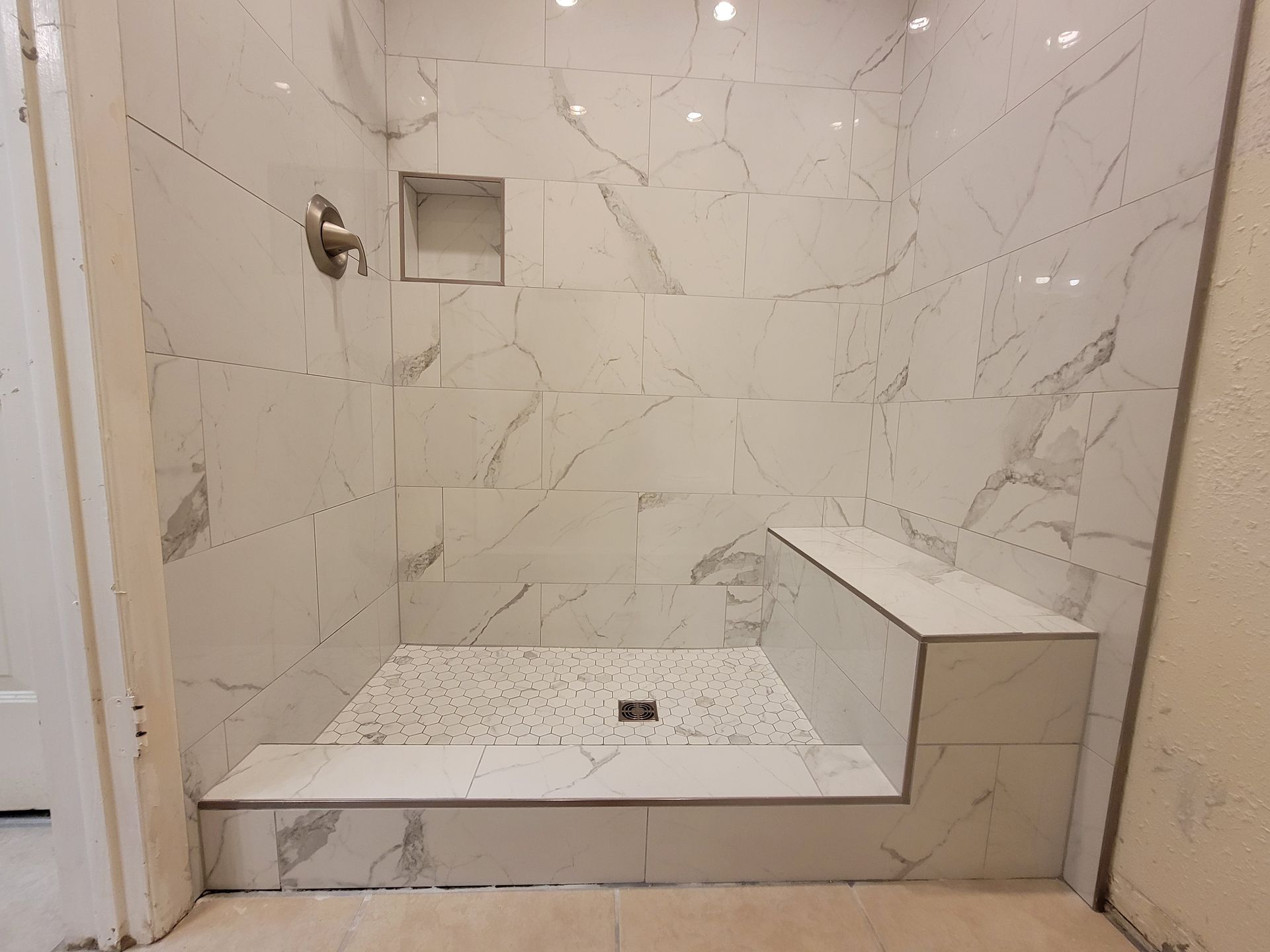 Tiled shower stall with a built-in seat and niche. White marble-look tiles.
