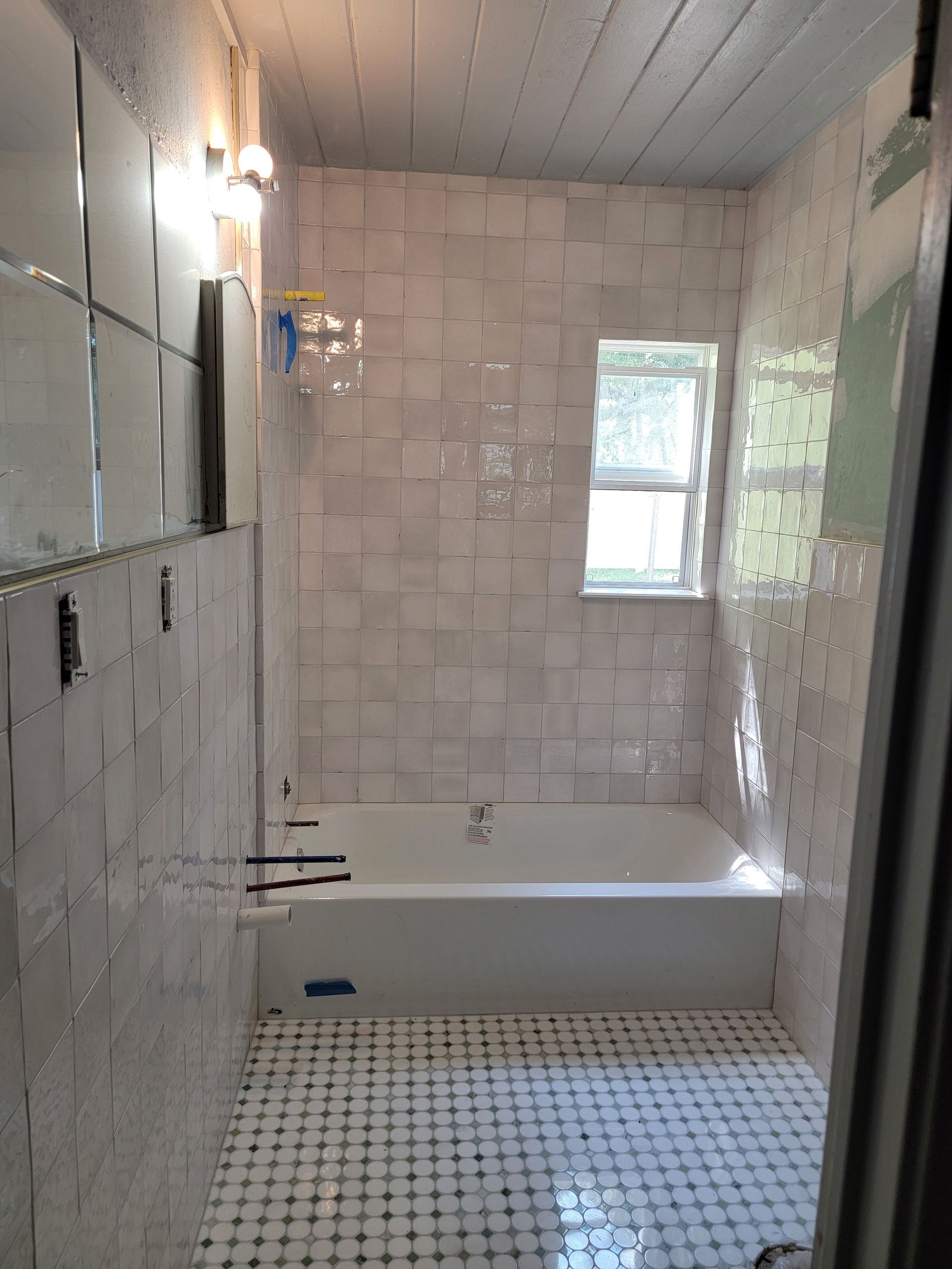 Newly tiled white bathroom with a bathtub, small window, and black and white tiled floor.