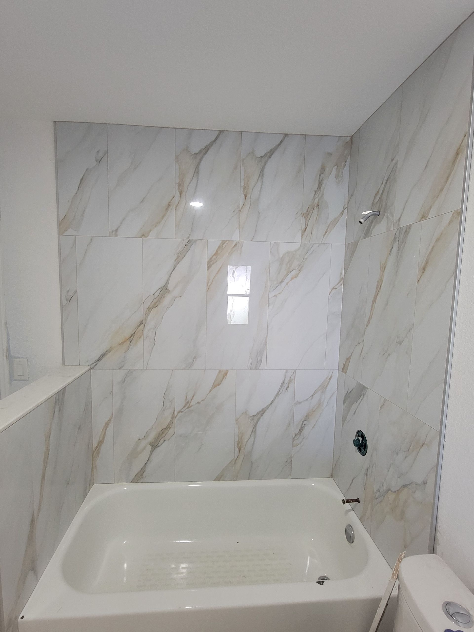 White bathtub with marble-patterned tile wall. Bathroom interior.