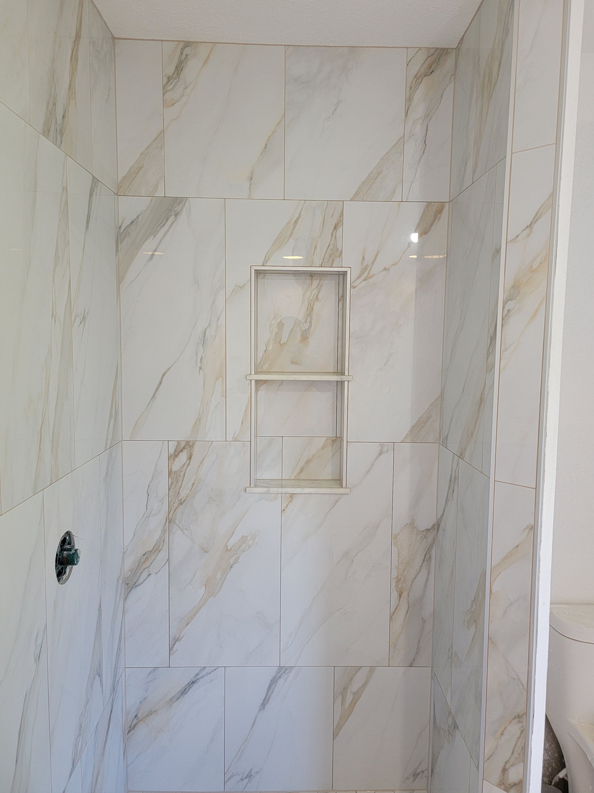 Tiled shower with a niche; white and gold marble-like pattern.