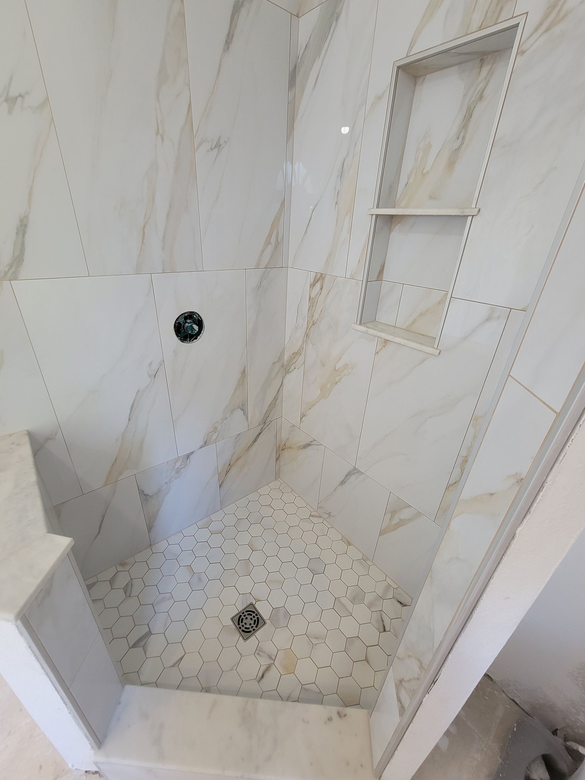 Tiled shower stall with white and gold marble-like tiles and a built-in shelf.