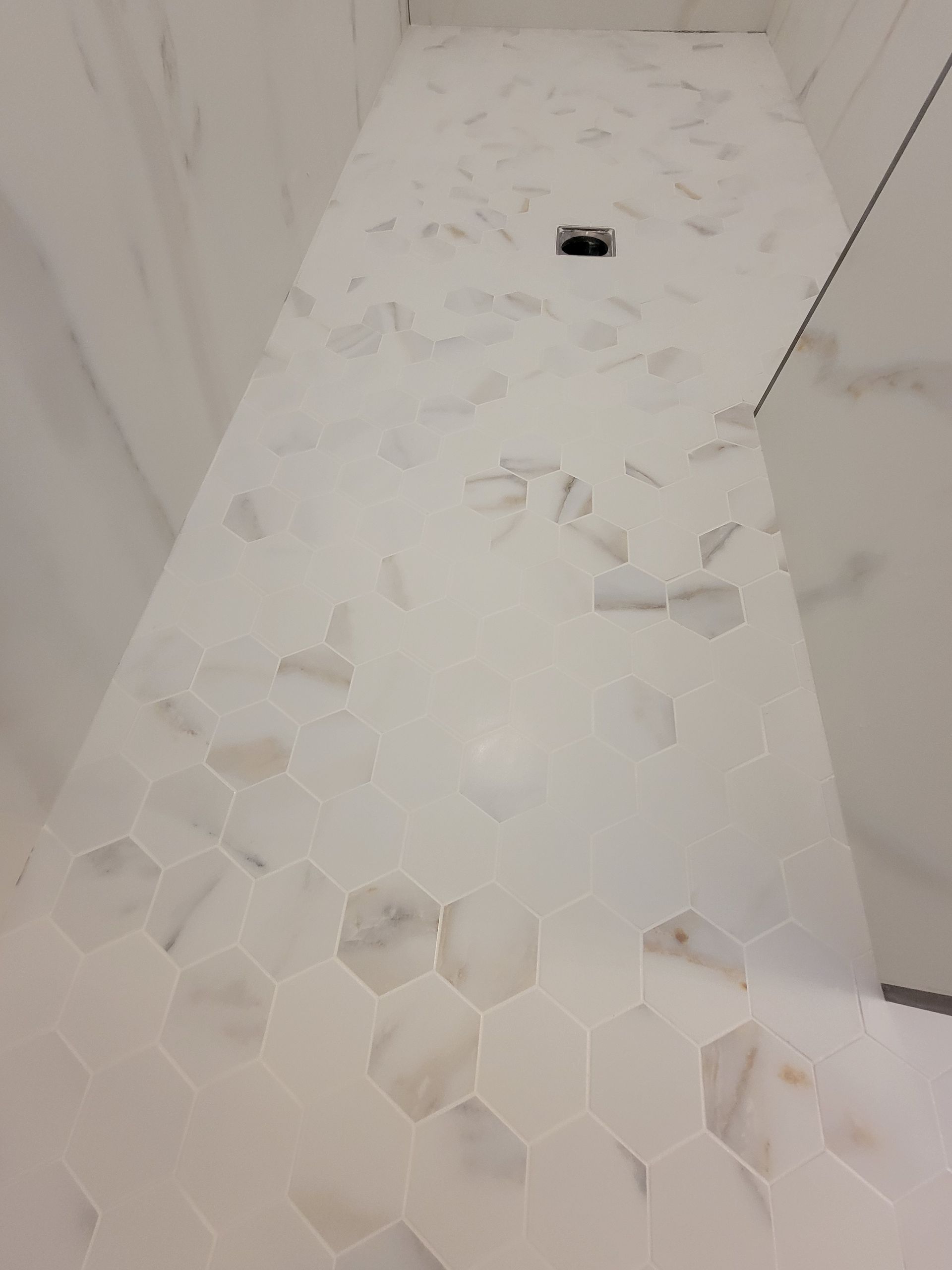 White and beige tiled shower floor with hexagonal and mosaic patterns, drain visible.
