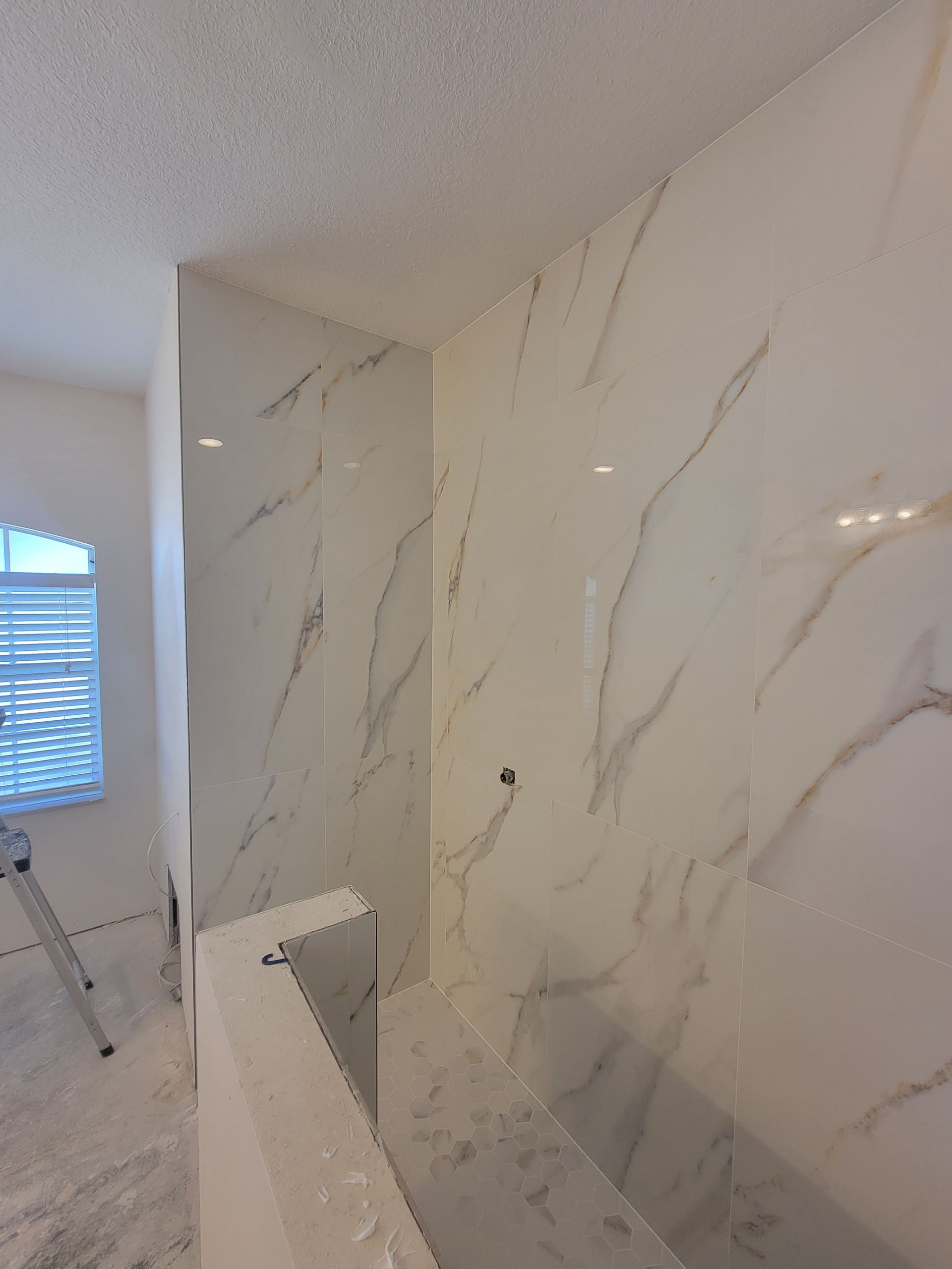 White marble tile walls in a bathroom with a window and a ledge.