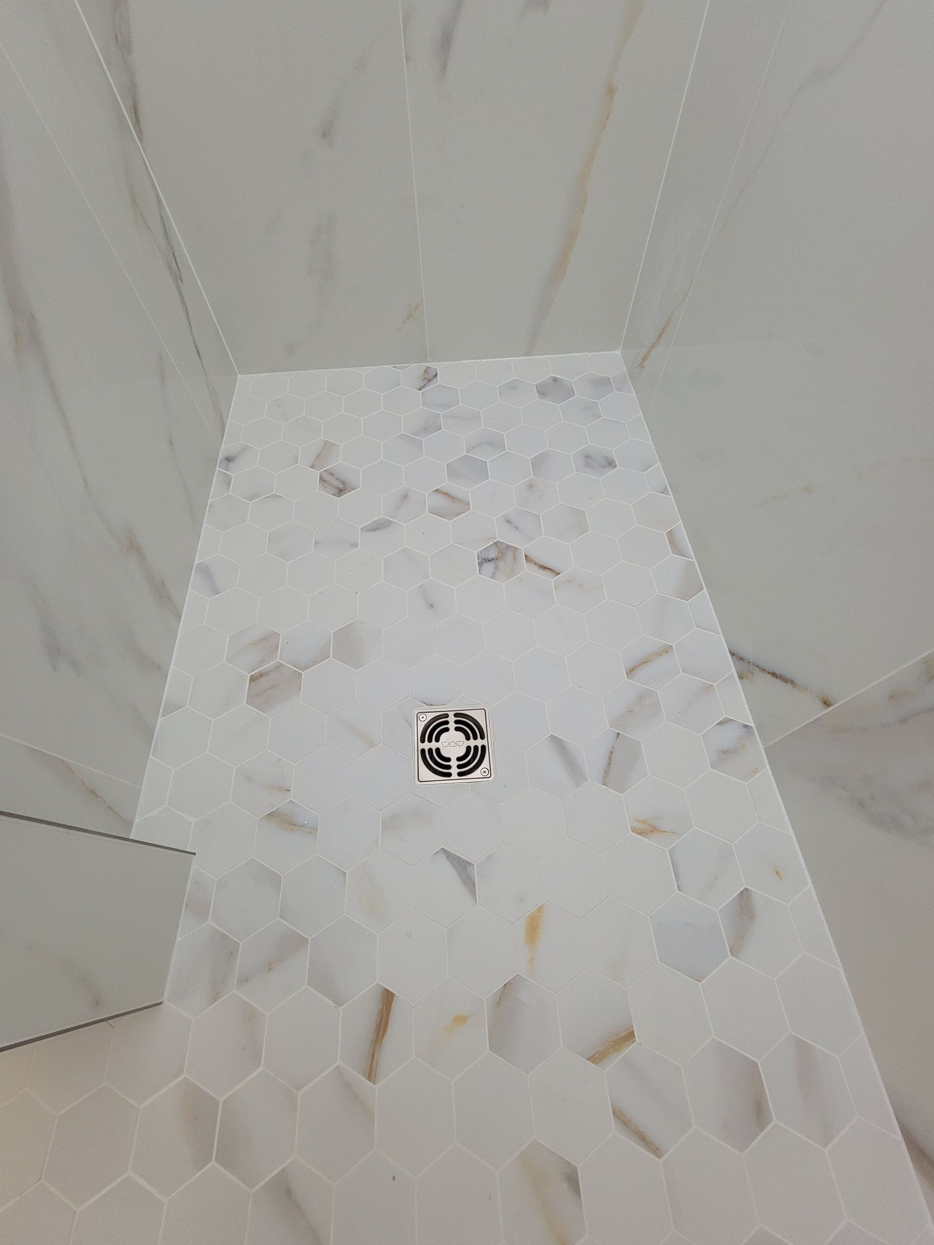 White tile shower floor with a central drain, surrounded by marble walls.