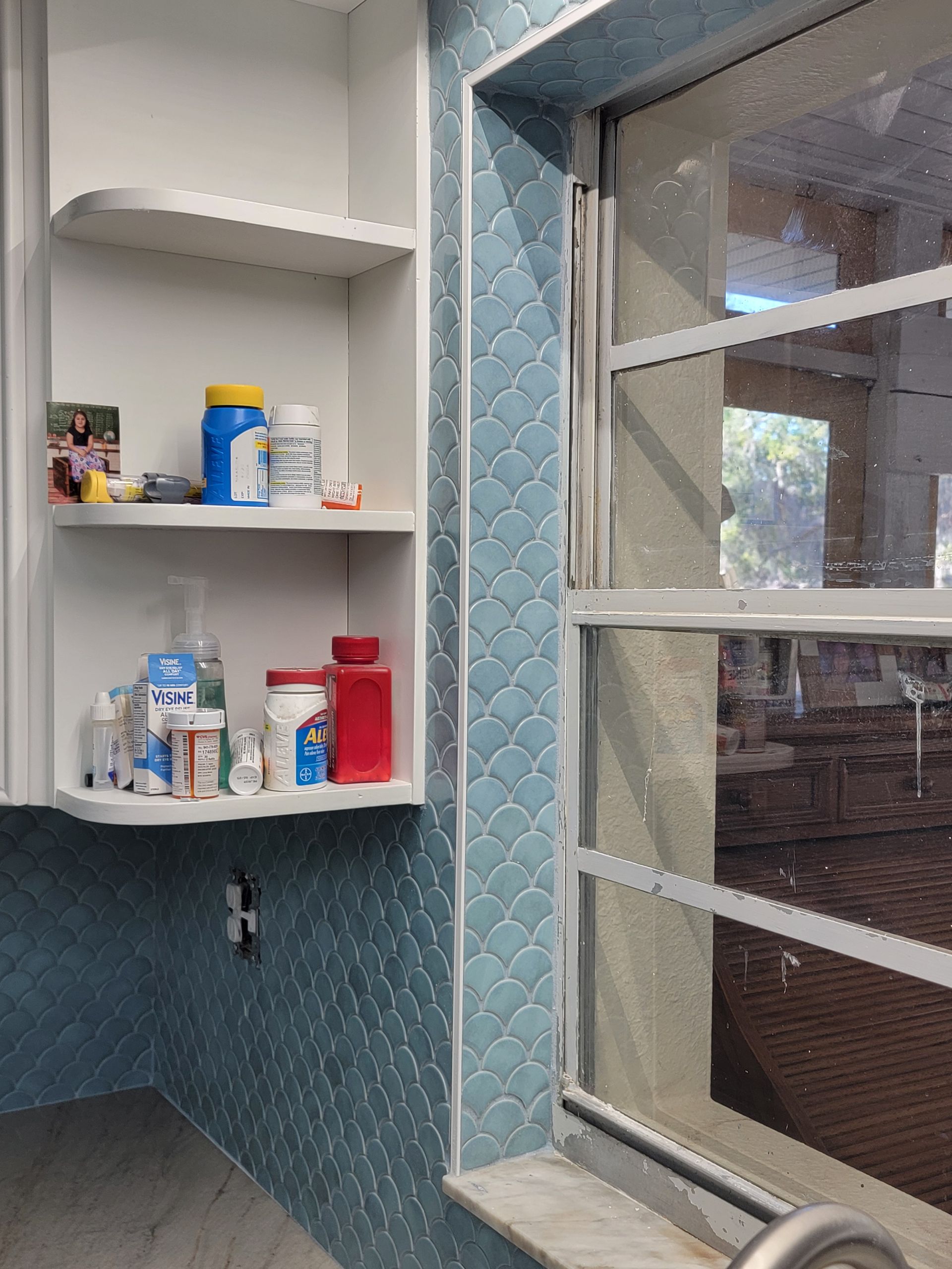 White cabinet with medications next to a window with blue tile backsplash.