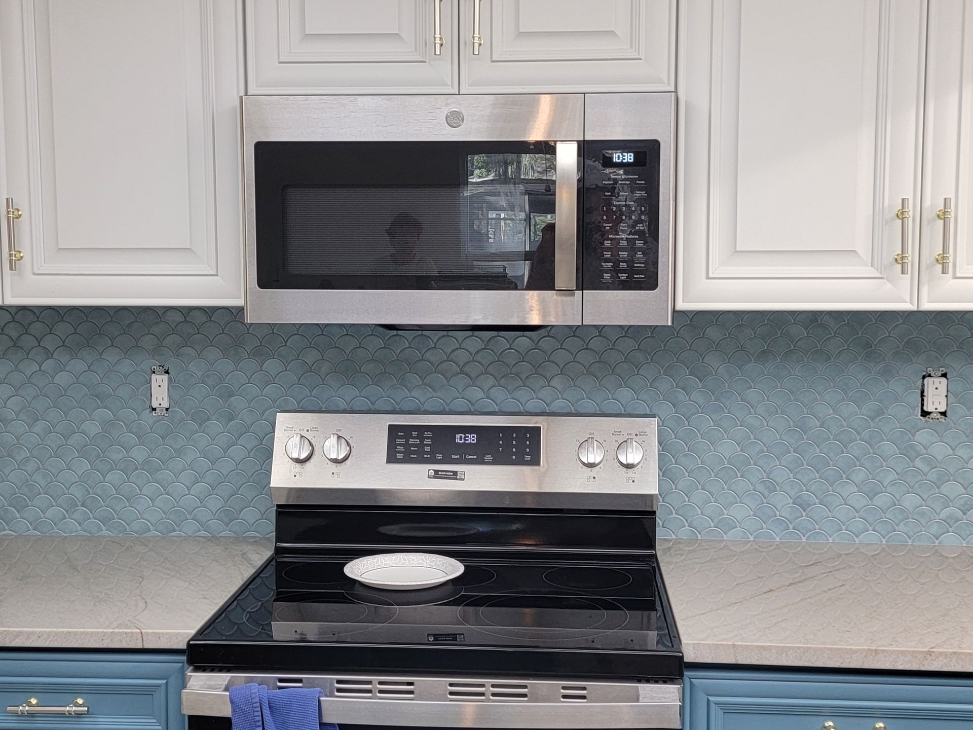 Kitchen with blue fish scale tile backsplash, stainless steel appliances, and white cabinets.